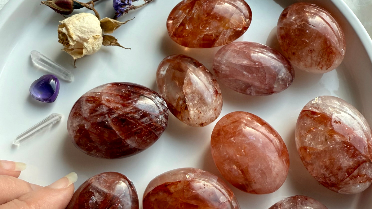 Fire Quartz palm stones with deep red hematite inclusions on white plate with amethyst heart and clear quartz points for grounding and healing energy