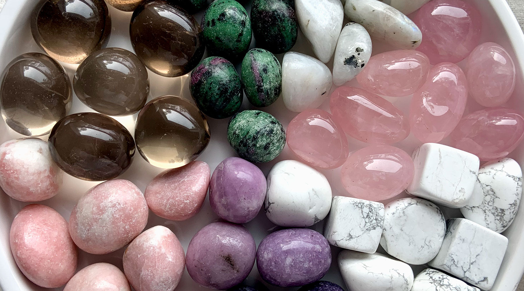 Comforting crystals for grief shown in closeup, including Rose Quartz, Smoky Quartz, Pink Opal, Lepidolite, Howlite, Rainbow Moonstone, and Ruby in Zoisite