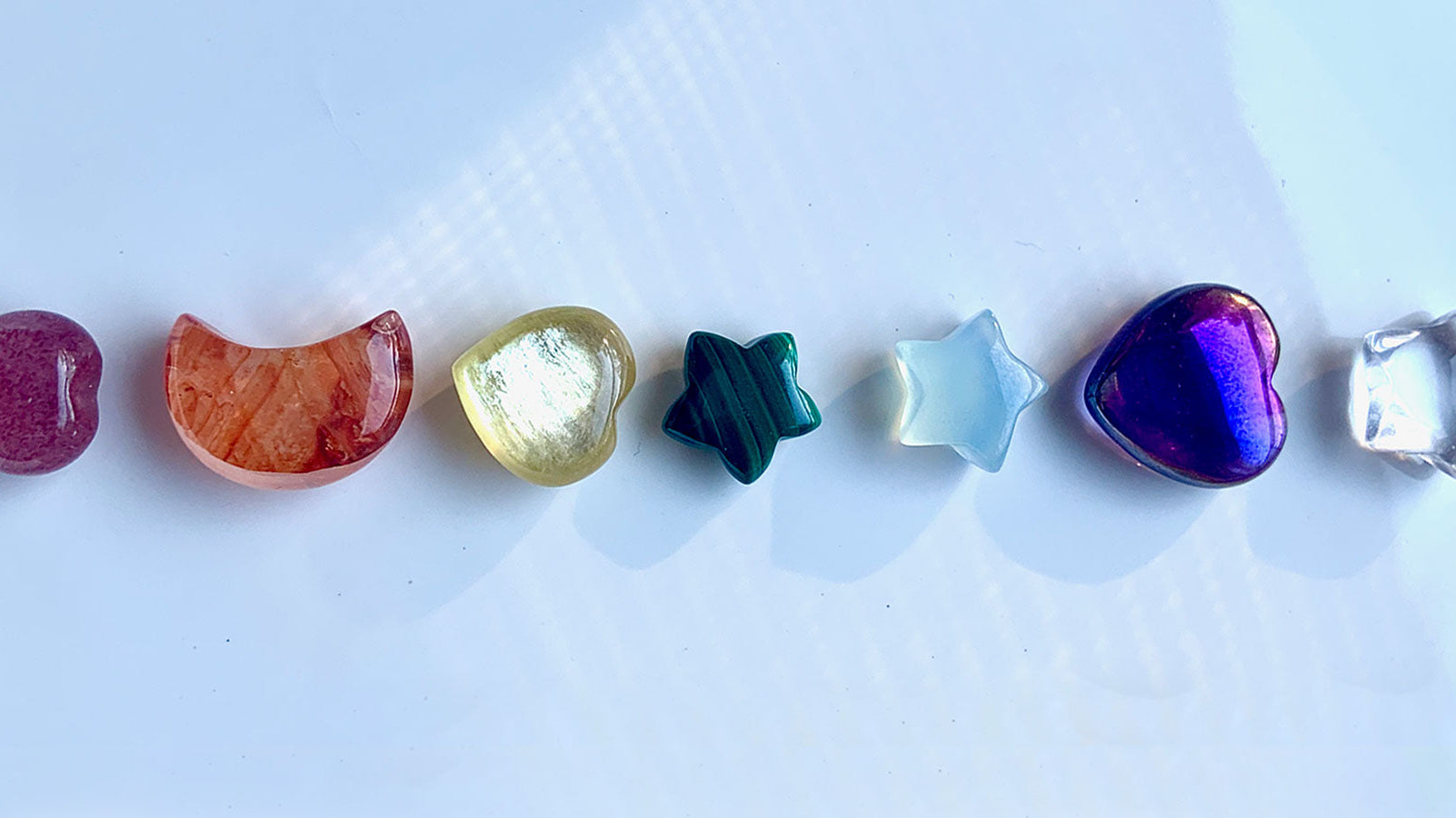 Chakra healing crystals banner featuring 7 mini gemstone carvings — heart, moon, star, and more — symbolizing the seven chakras for balance, alignment, and energy healing.