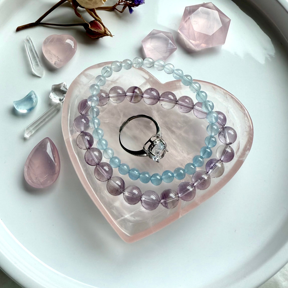 Healing crystal jewelry styled in a rose quartz heart bowl featuring crystal bracelets and a clear quartz ring for energy alignment, protection, and spiritual style
