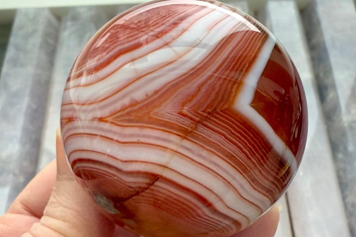 Closeup of a polished Carnelian crystal sphere with vivid orange and white swirling stripes — grounding Root and Sacral Chakra stone for energy, vitality, and creativity.
