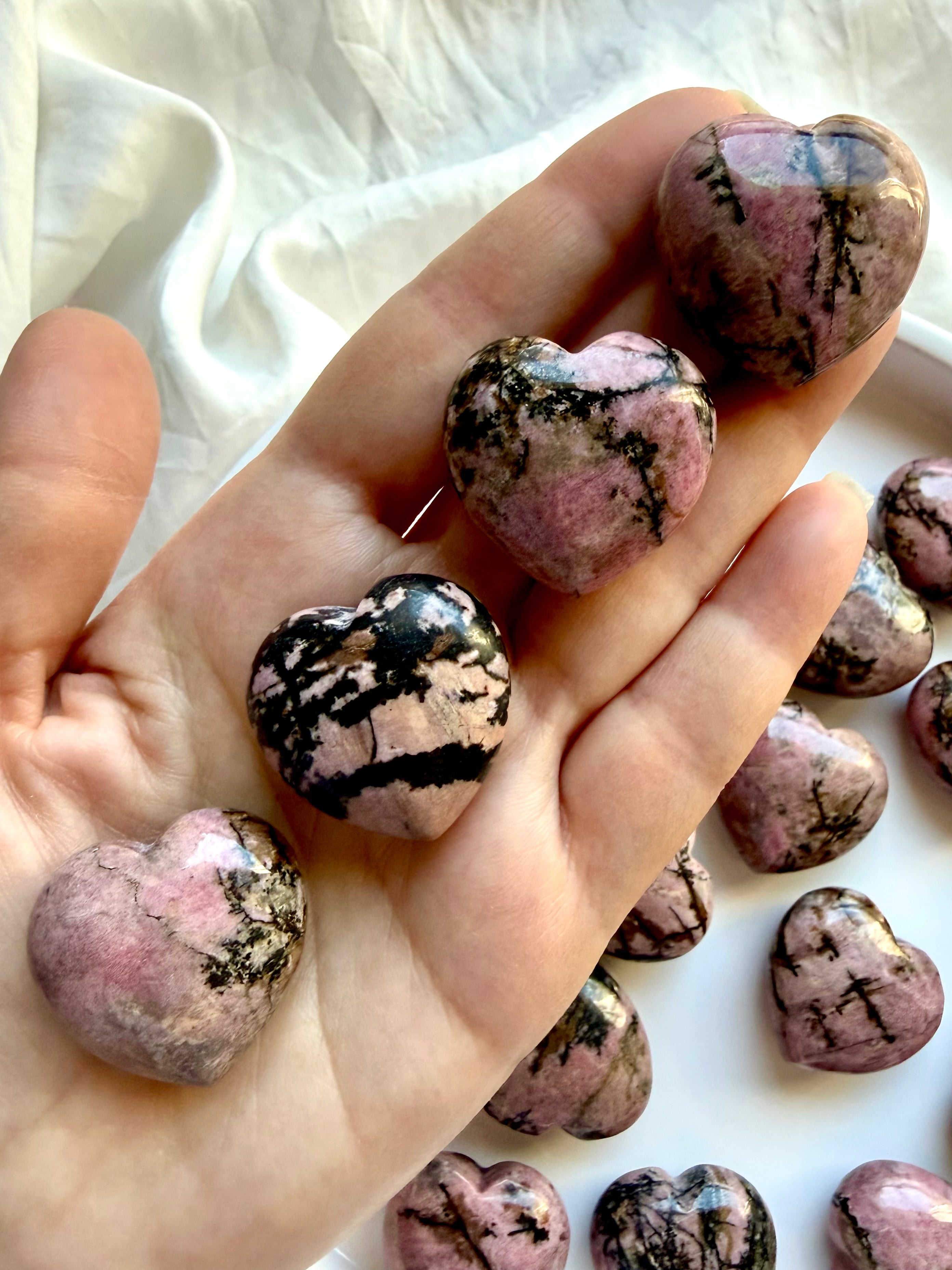 Rhodonite crystal hearts held in hand showing unique pink, black and earthy natural patterns