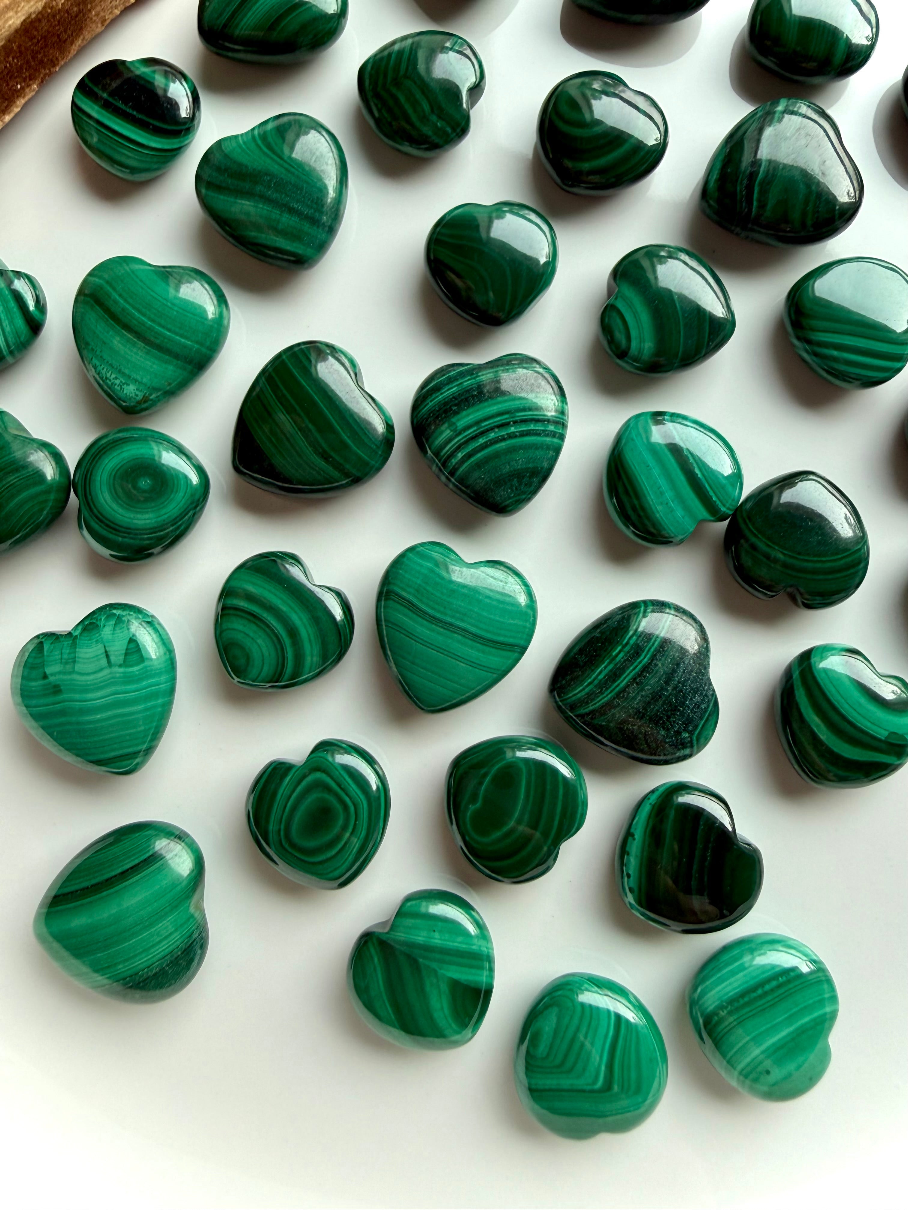 Close-up of polished Malachite heart carvings showing rich banded patterns in vibrant green tones.