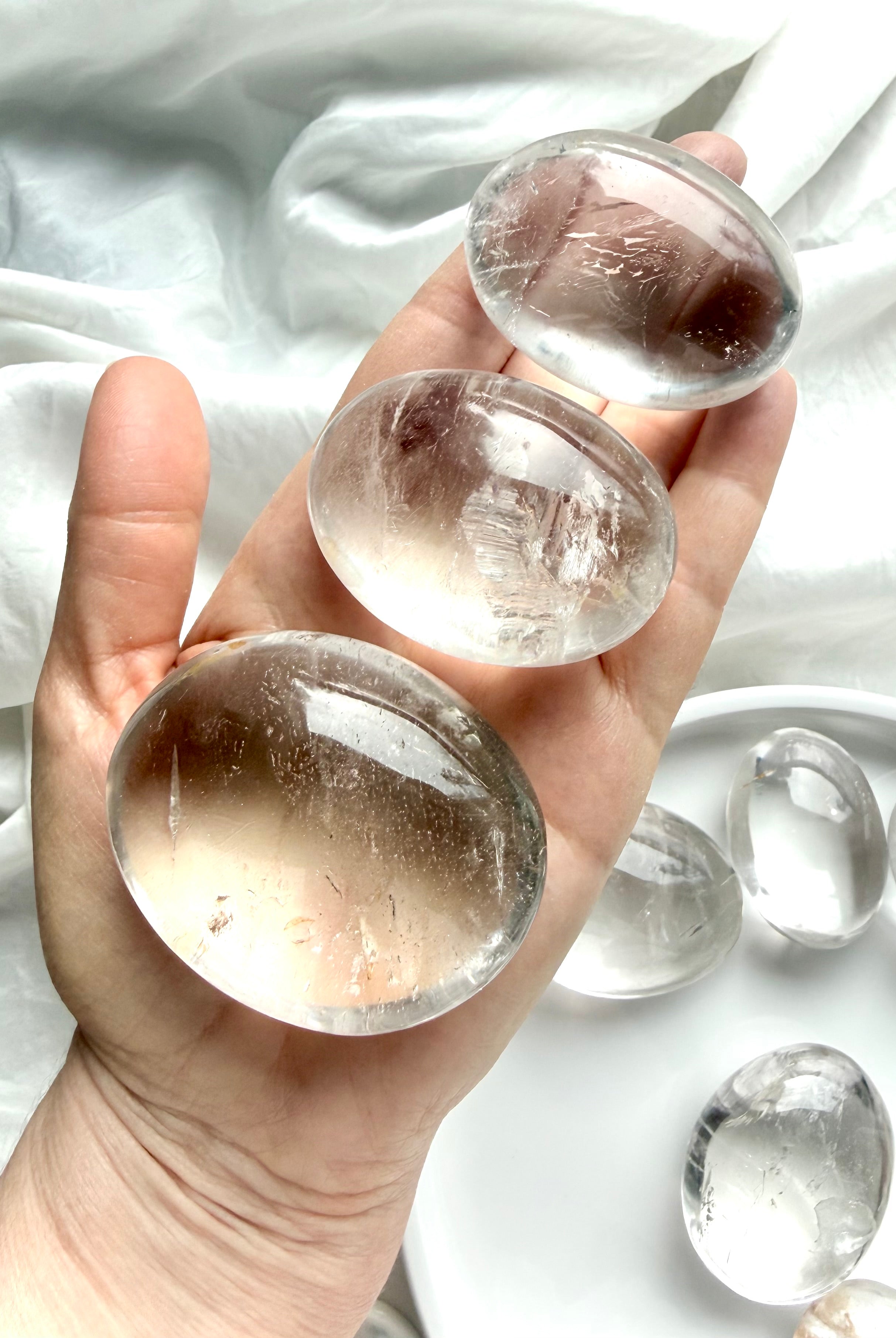 three clear quartz palm stones held in hand with high clarity, silvery flashes, and natural inclusions