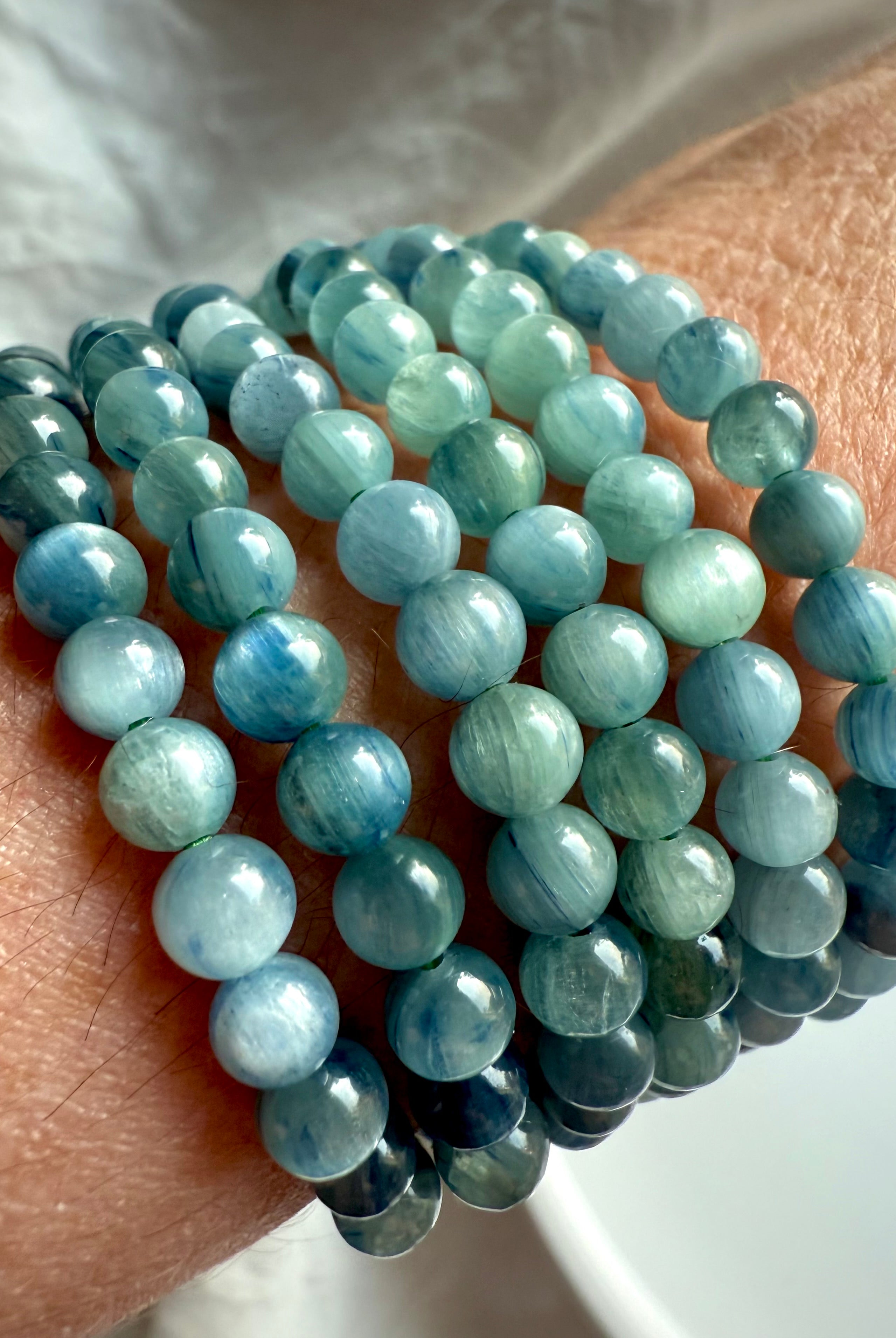angled view of stacked blue-green kyanite crystal bracelets on wrist, displaying natural shimmer, layered texture, and calming chakra colors for energetic balance