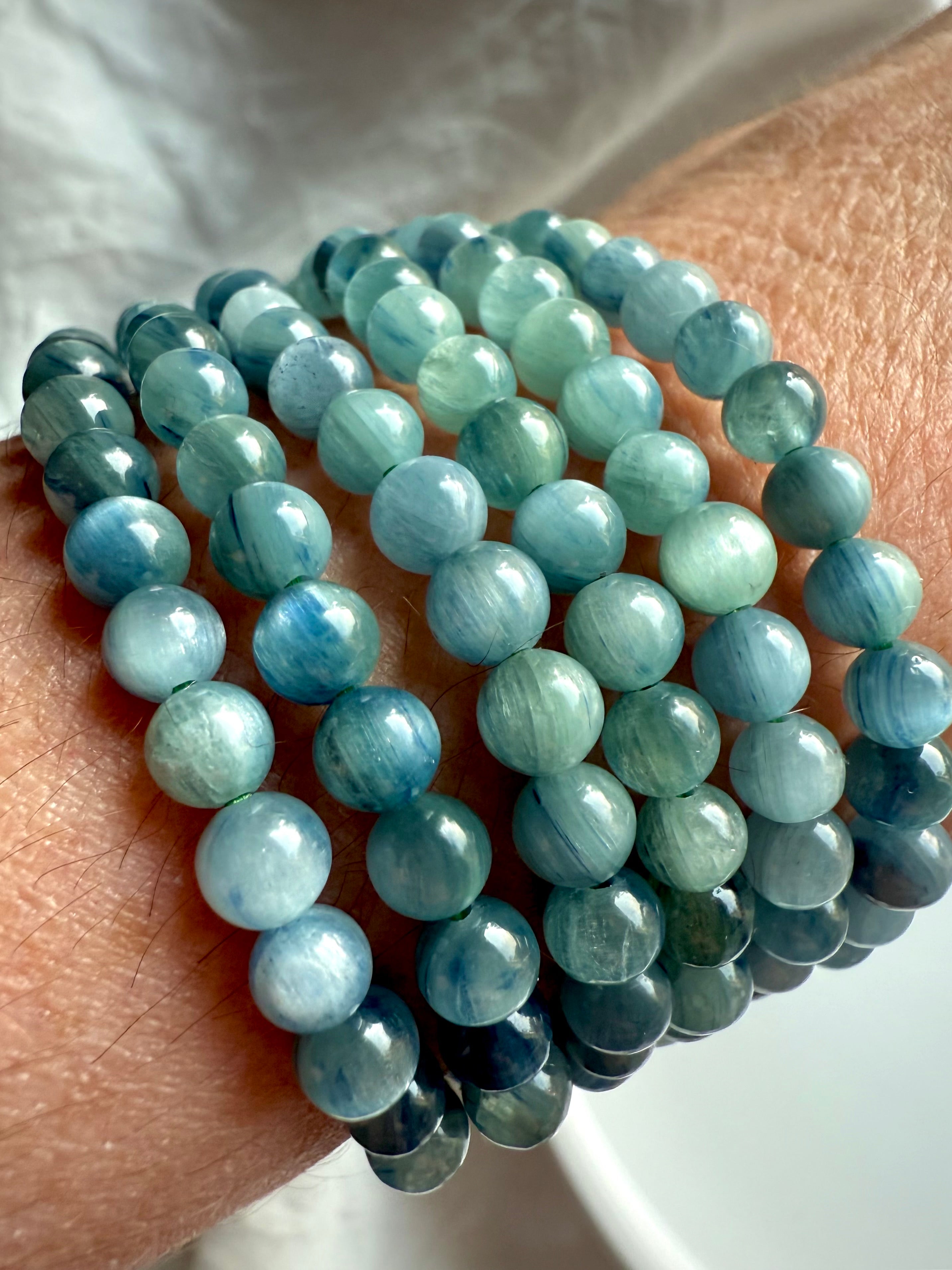 angled view of stacked blue-green kyanite crystal bracelets on wrist, displaying natural shimmer, layered texture, and calming chakra colors for energetic balance