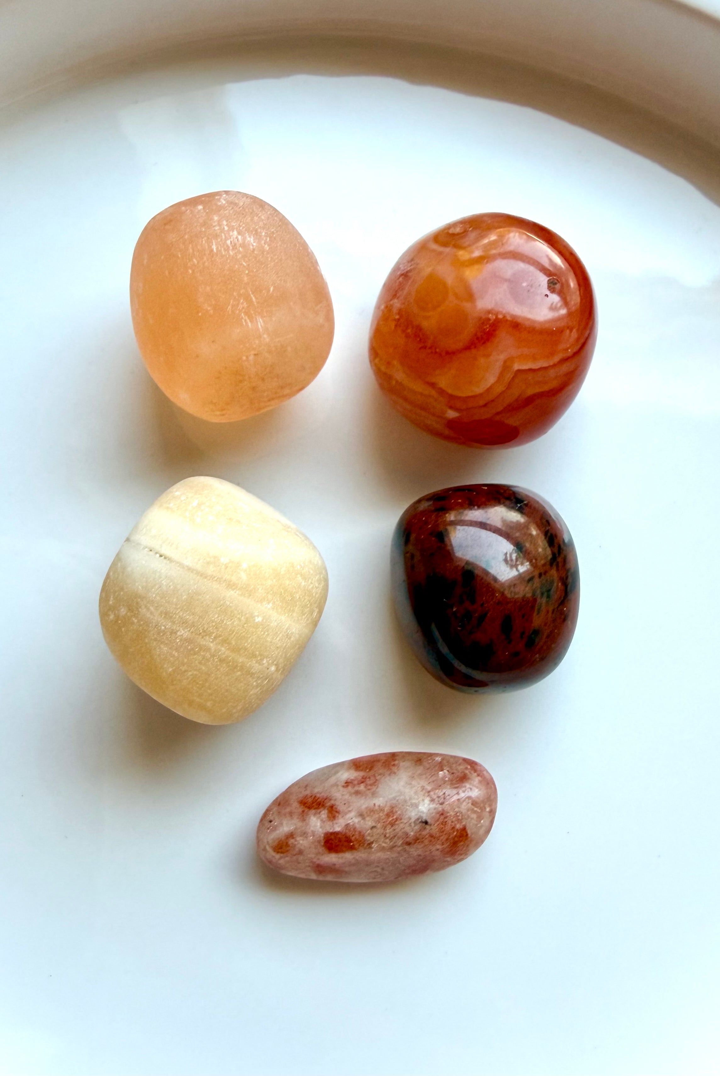 Five polished Sacral Chakra stones including Orange Calcite, Carnelian, Peach Selenite, Mahogany Obsidian, and Sunstone