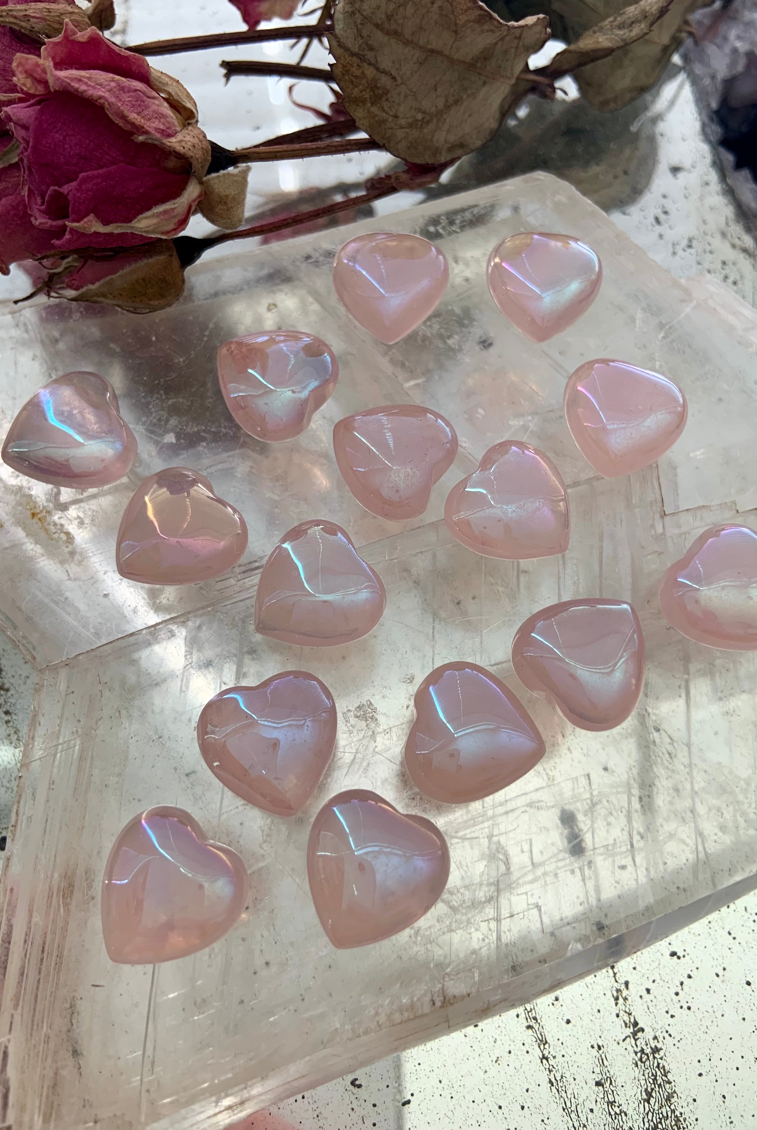 Mini aura rose quartz hearts on a selenite slab with dried roses — glowing pink crystals for love, healing & heart-centered rituals