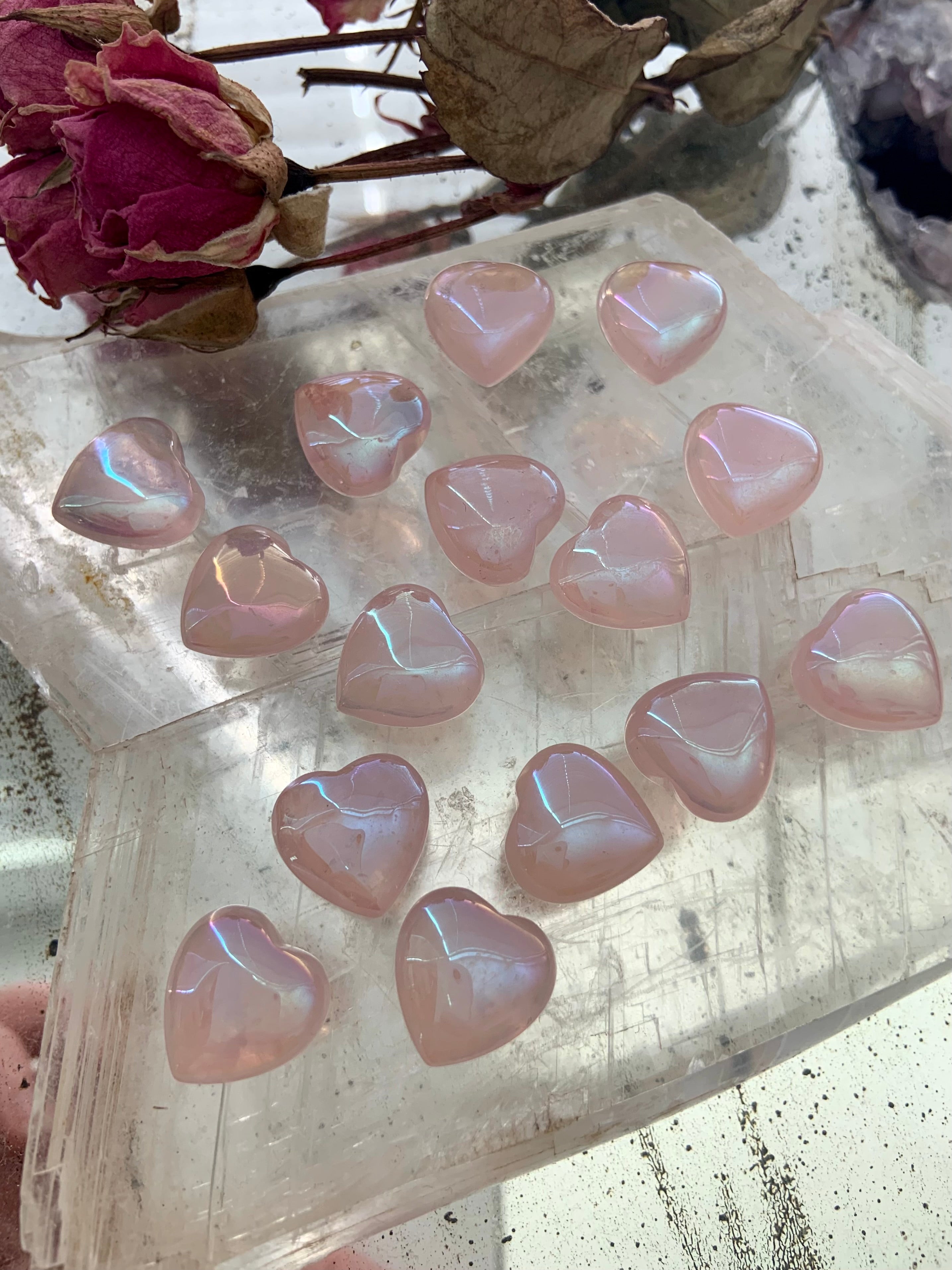 Mini aura rose quartz hearts on a selenite slab with dried roses — glowing pink crystals for love, healing & heart-centered rituals