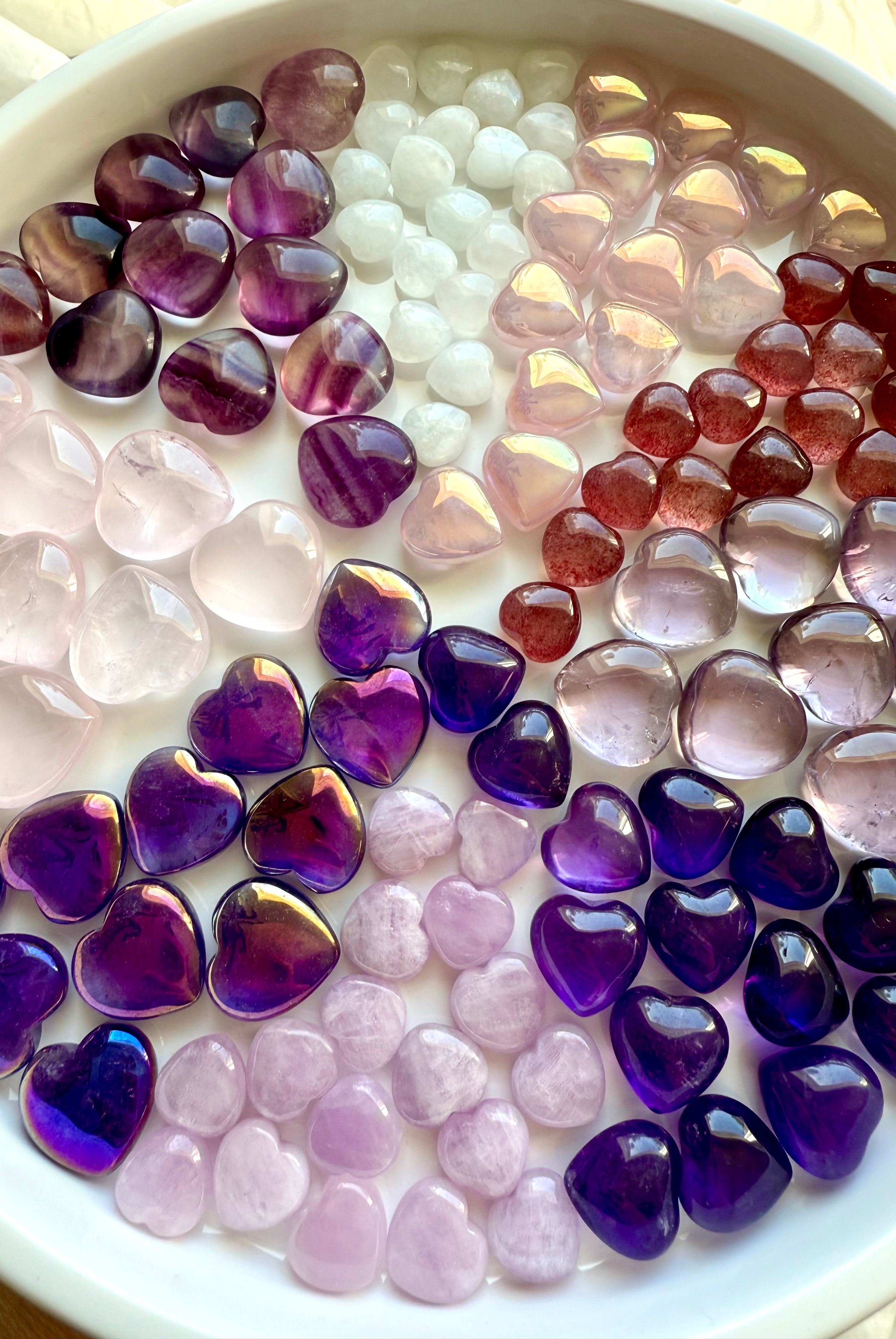 Multiple pink and purple mini crystal hearts arranged in pie-slice formation by stone type, premium carved gemstone hearts.