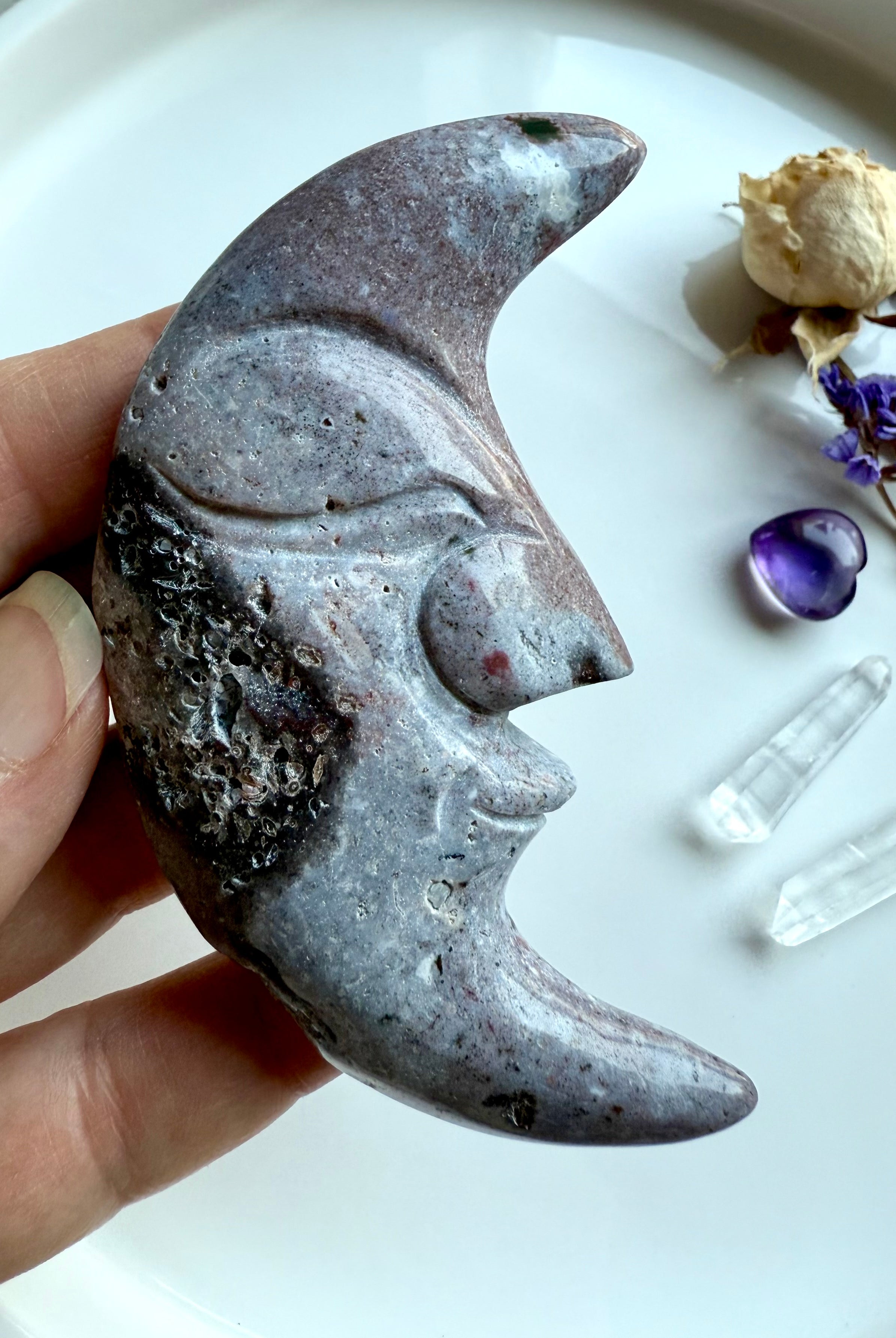 Purple Ocean Jasper moon face crystal with druzy detail, displayed beside quartz points, amethyst, and flowers.