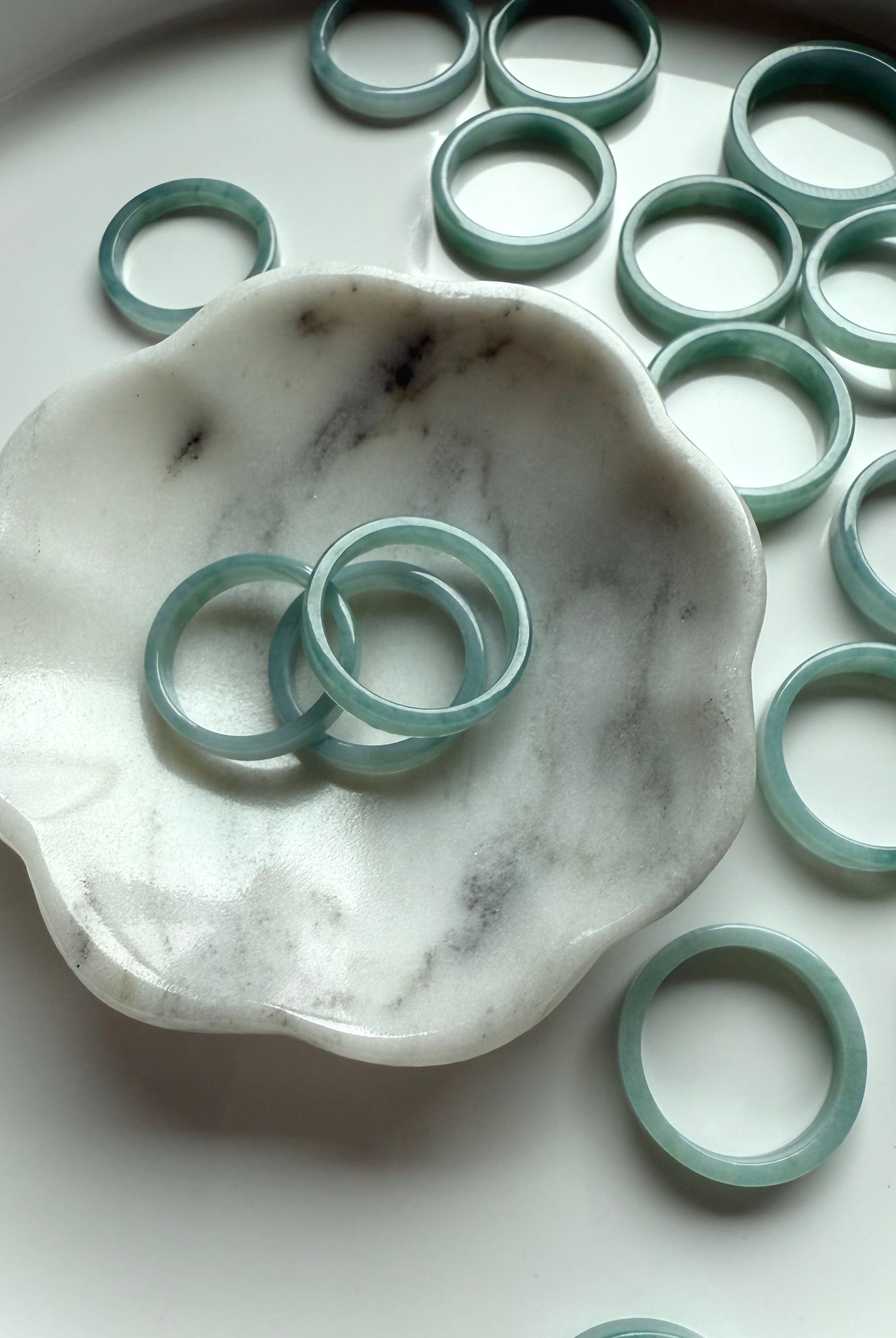 Flat jadeite rings in a serene aqua tone displayed around a white and gray marble jewelry dish