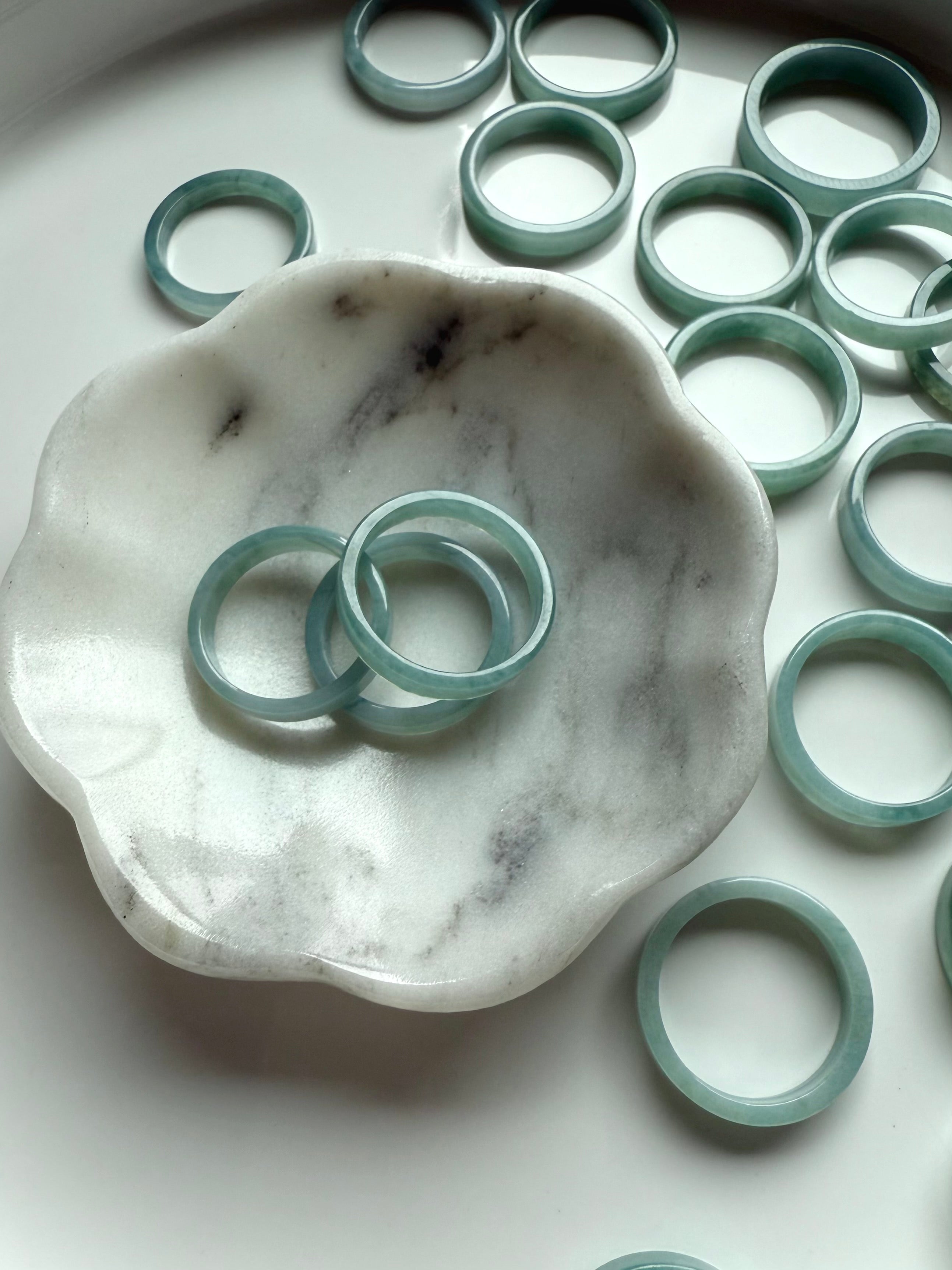 Flat jadeite rings in a serene aqua tone displayed around a white and gray marble jewelry dish