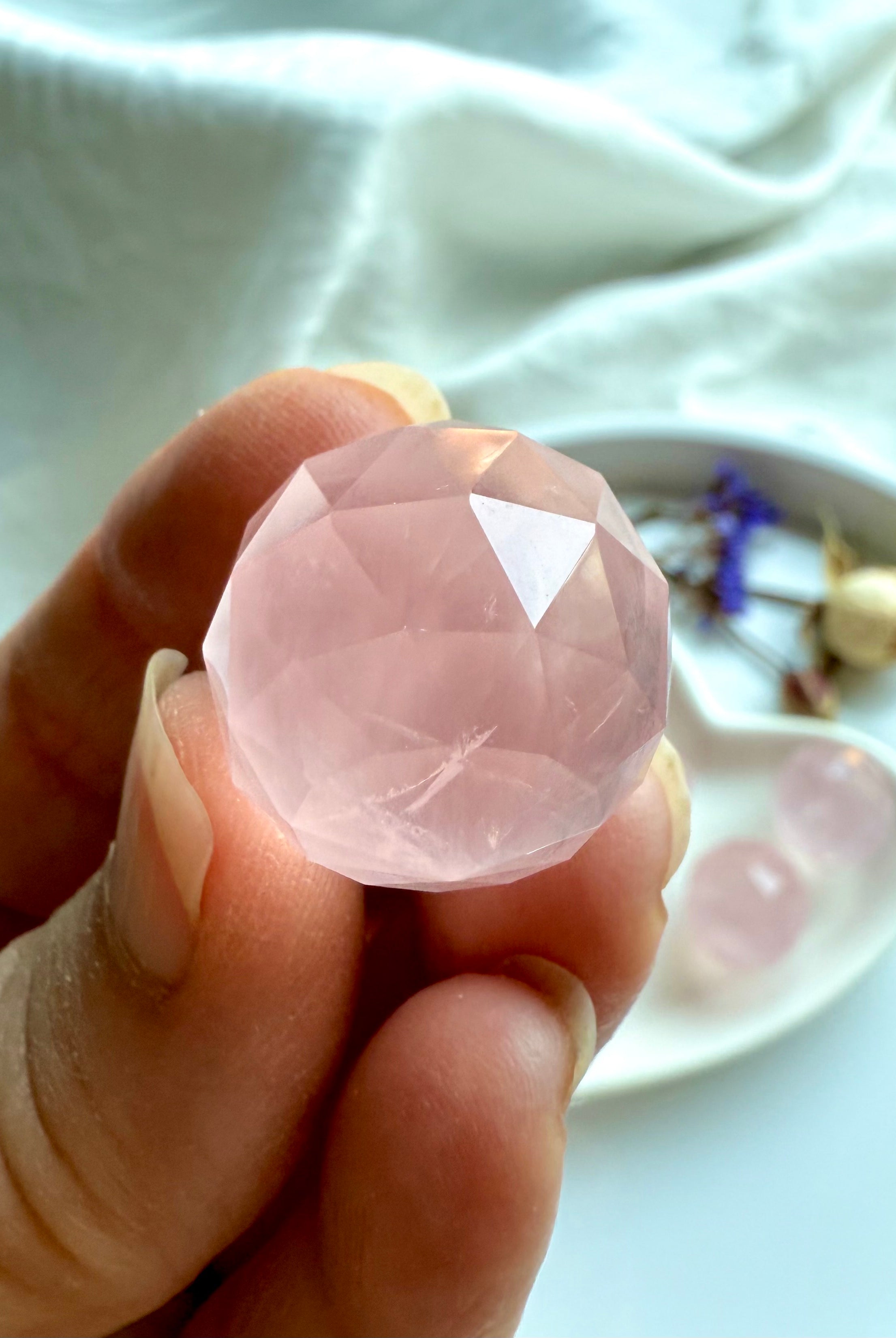 Closeup of a hand showing the intricate details of a mini faceted rose quartz crystal ball.