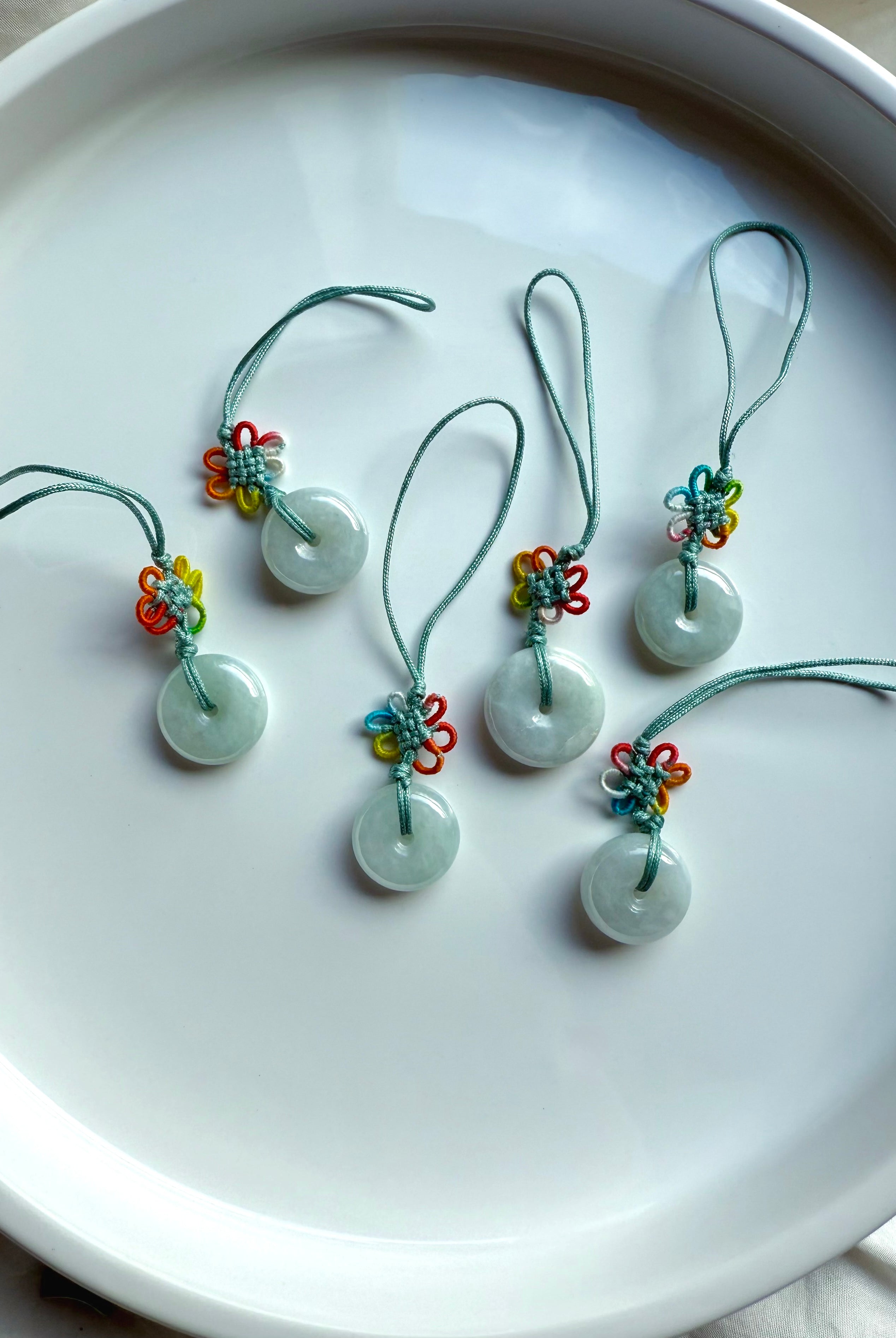 Natural jade donut talismans with rainbow flower knots displayed in a crescent fan shape