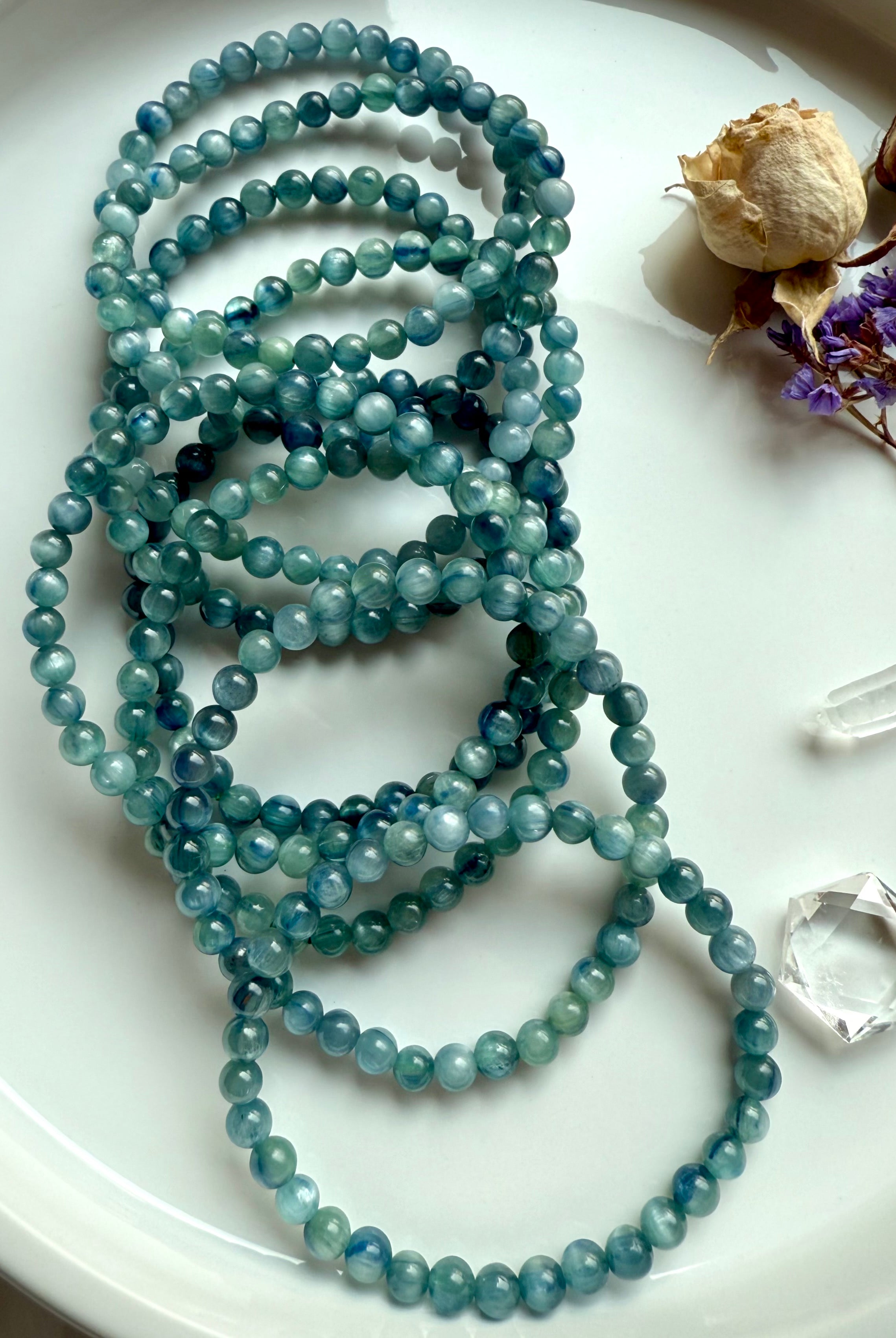 overhead photo of multiple kyanite bracelets on a plate with rich variation of teal, turquoise, and earthy ocean hues