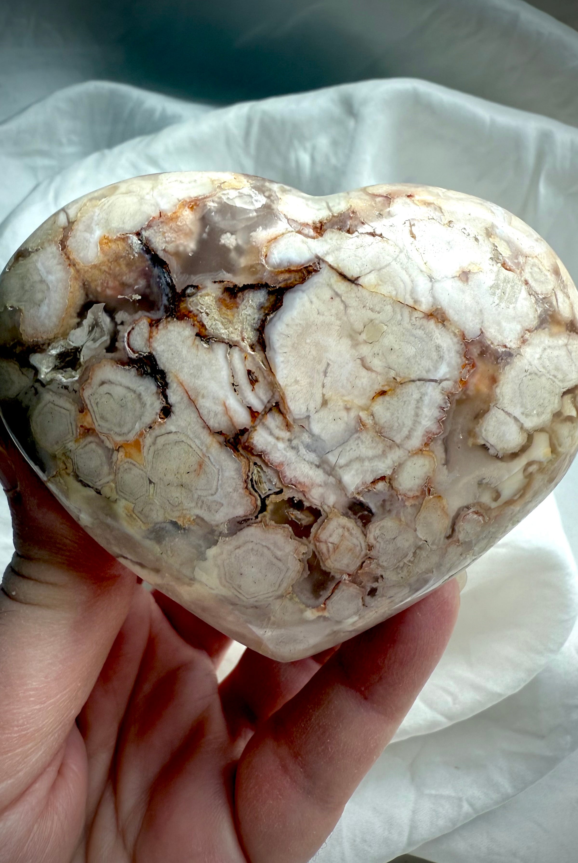 Flower Agate heart held in the palm, showcasing soft blooming patterns and pastel chalcedony — nurturing crystal for emotional healing and heart chakra balance.