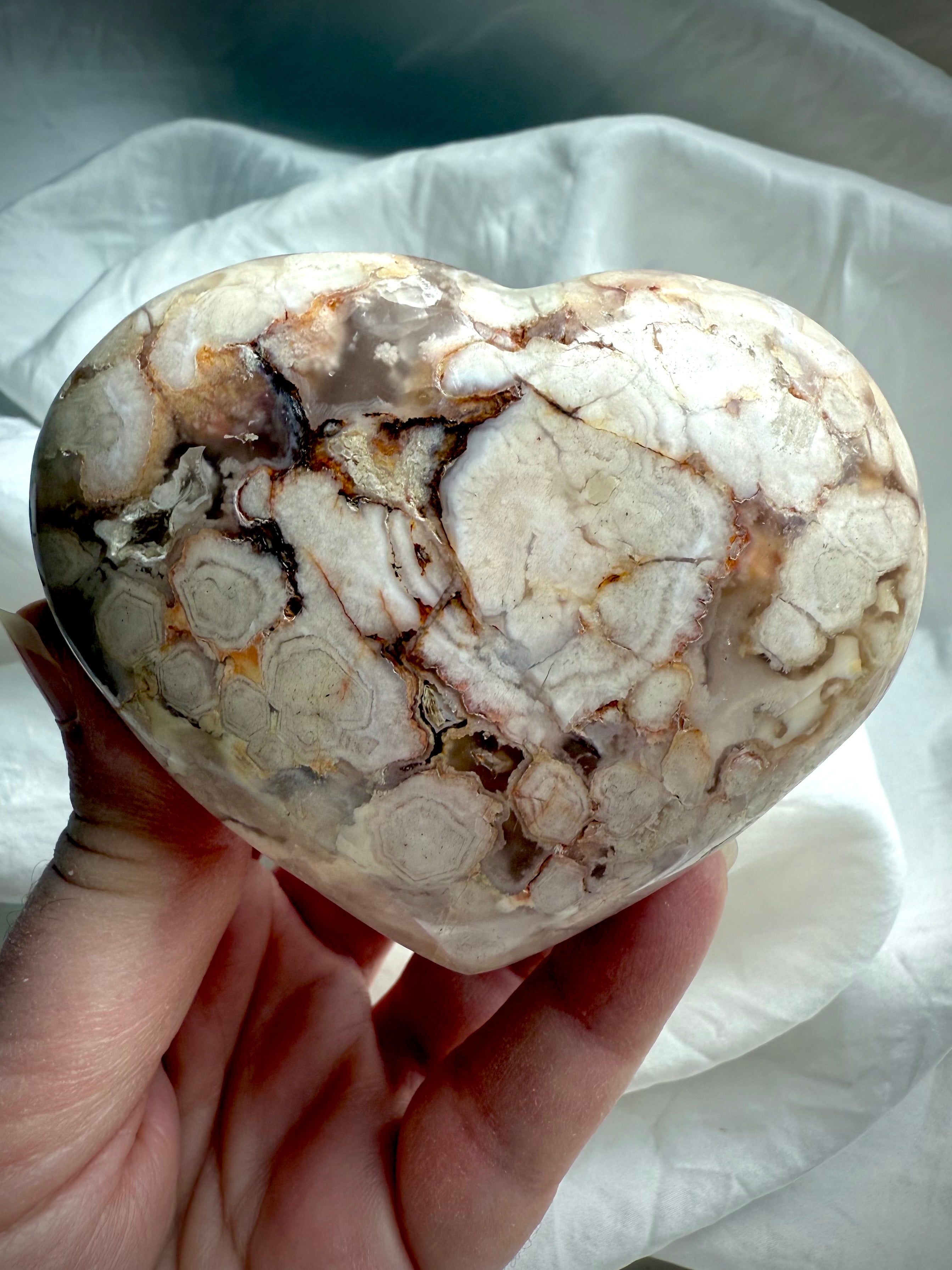 Flower Agate heart held in the palm, showcasing soft blooming patterns and pastel chalcedony โ nurturing crystal for emotional healing and heart chakra balance.