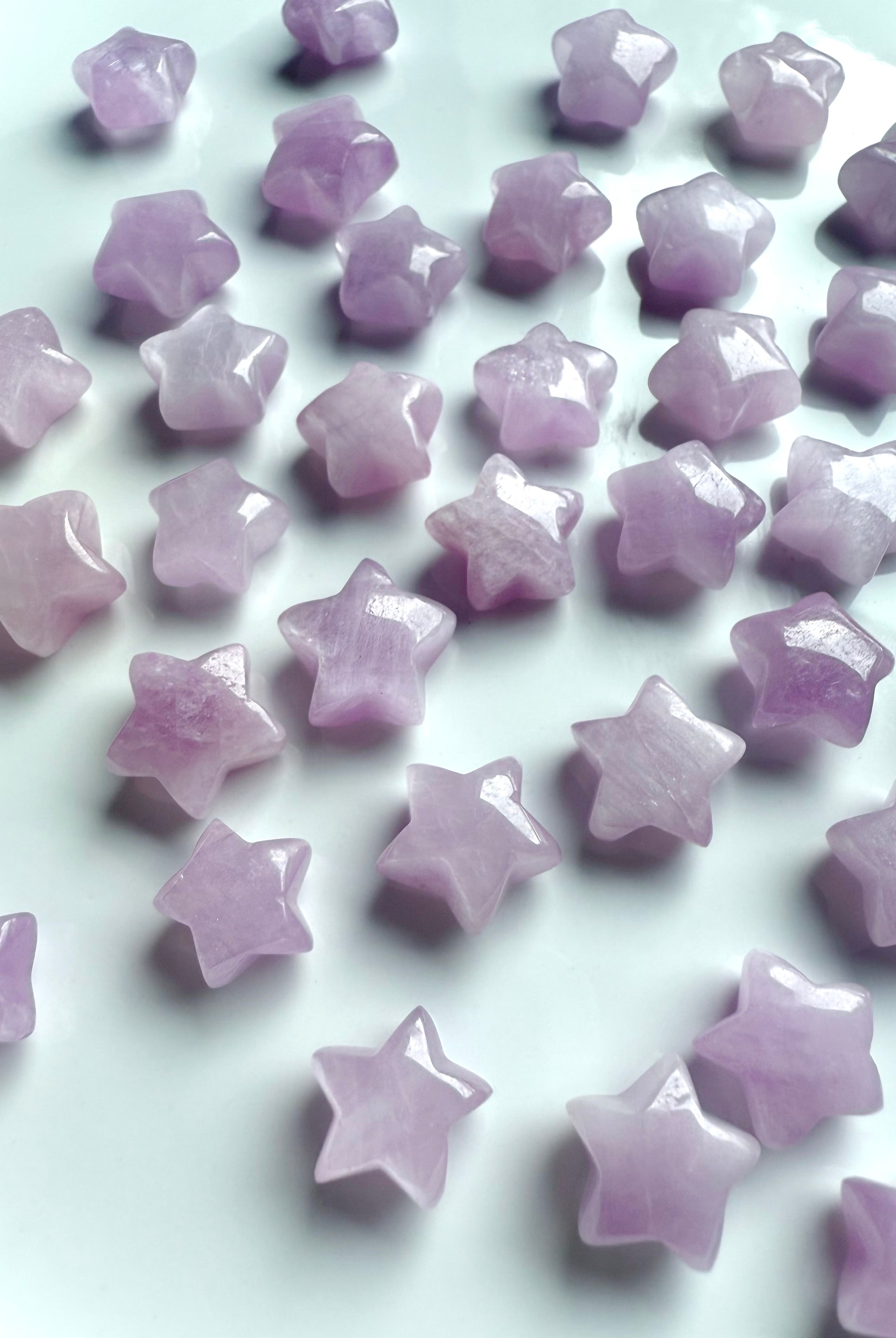 Closeup of pink Kunzite star carvings scattered on a white background, highlighting their glossy polish and soft shimmer.