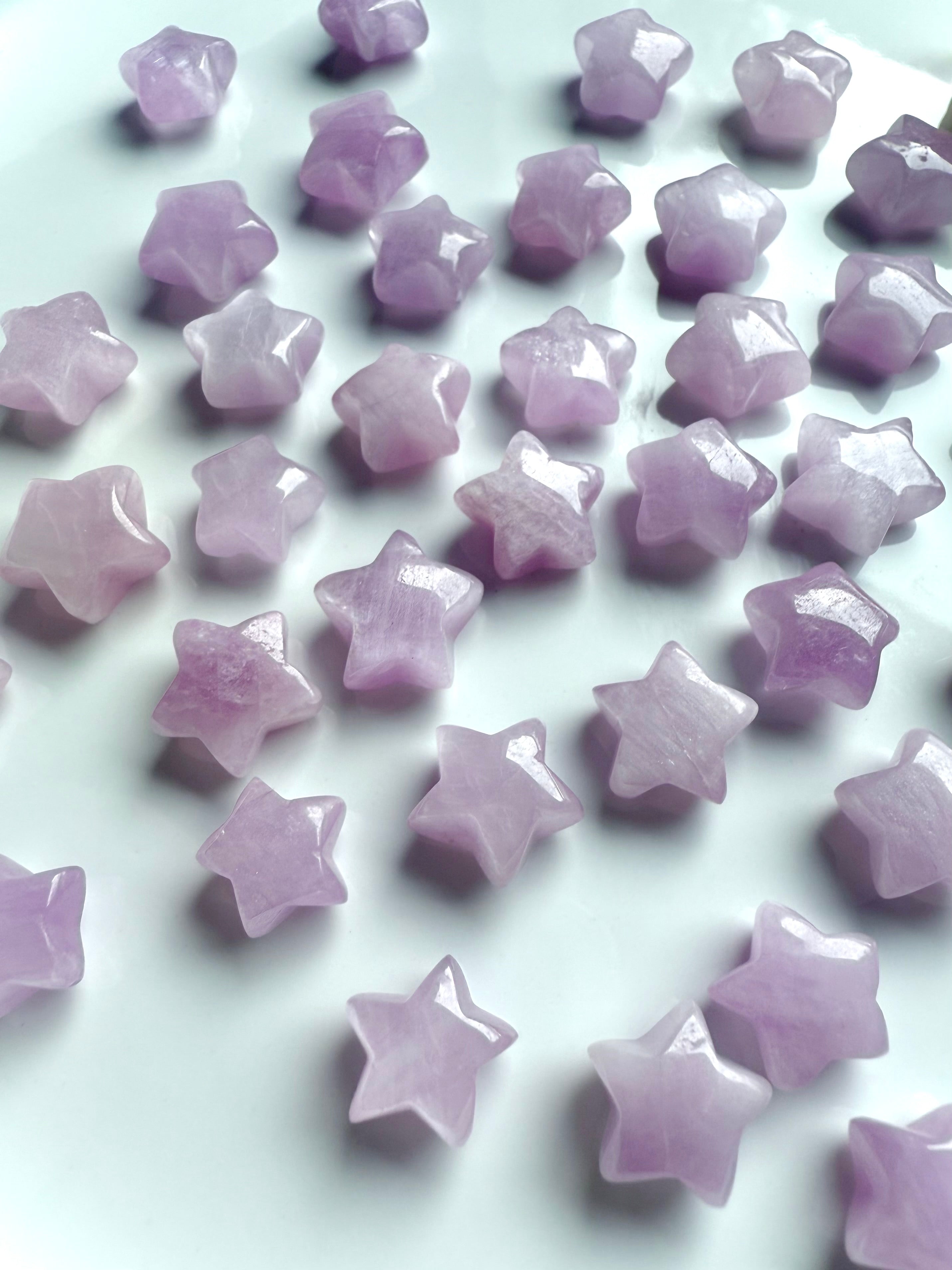 Closeup of pink Kunzite star carvings scattered on a white background, highlighting their glossy polish and soft shimmer.