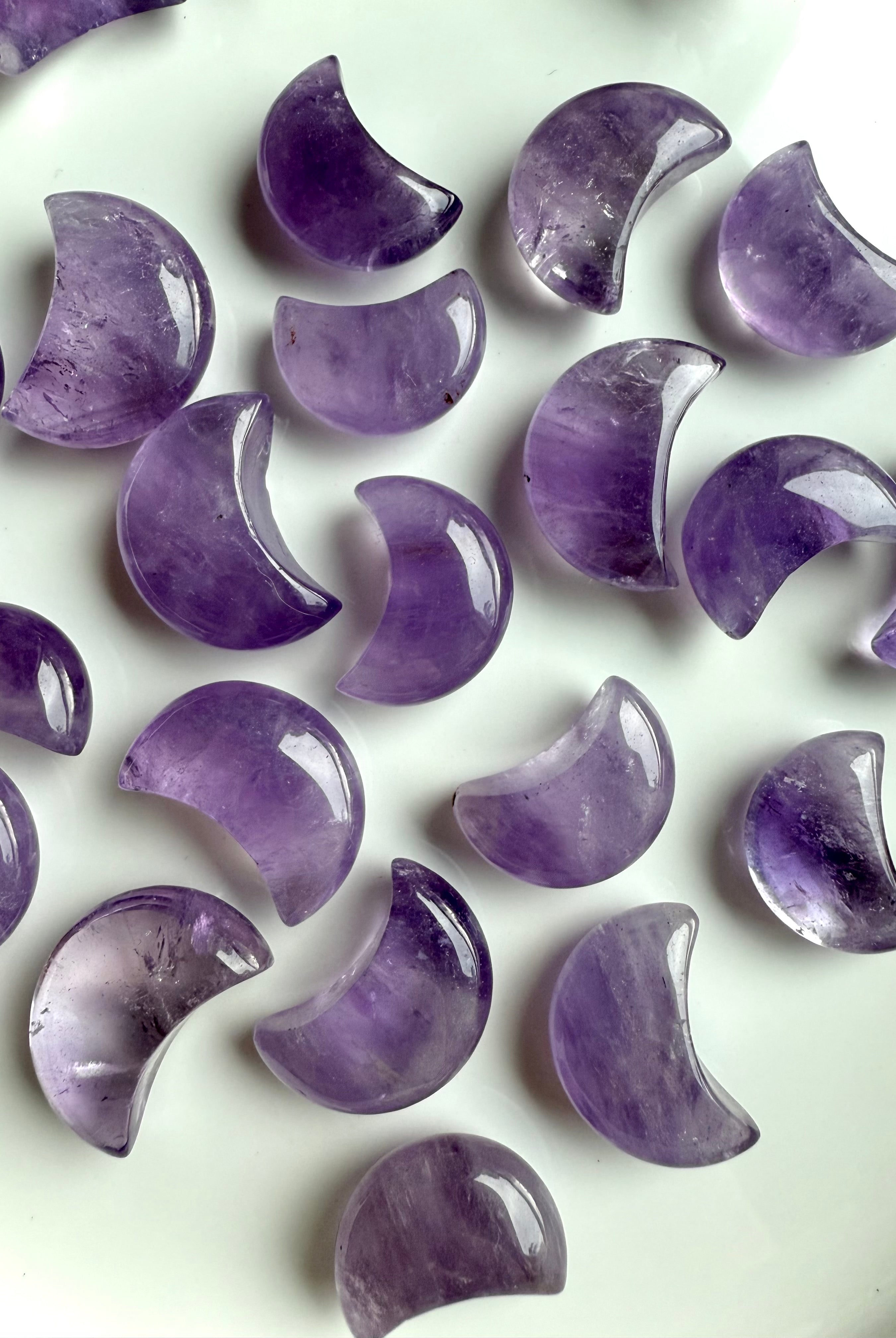 Mini amethyst crescent moon carvings in soft lavender and deep violet shades, polished crystal moons arranged on a white surface.
