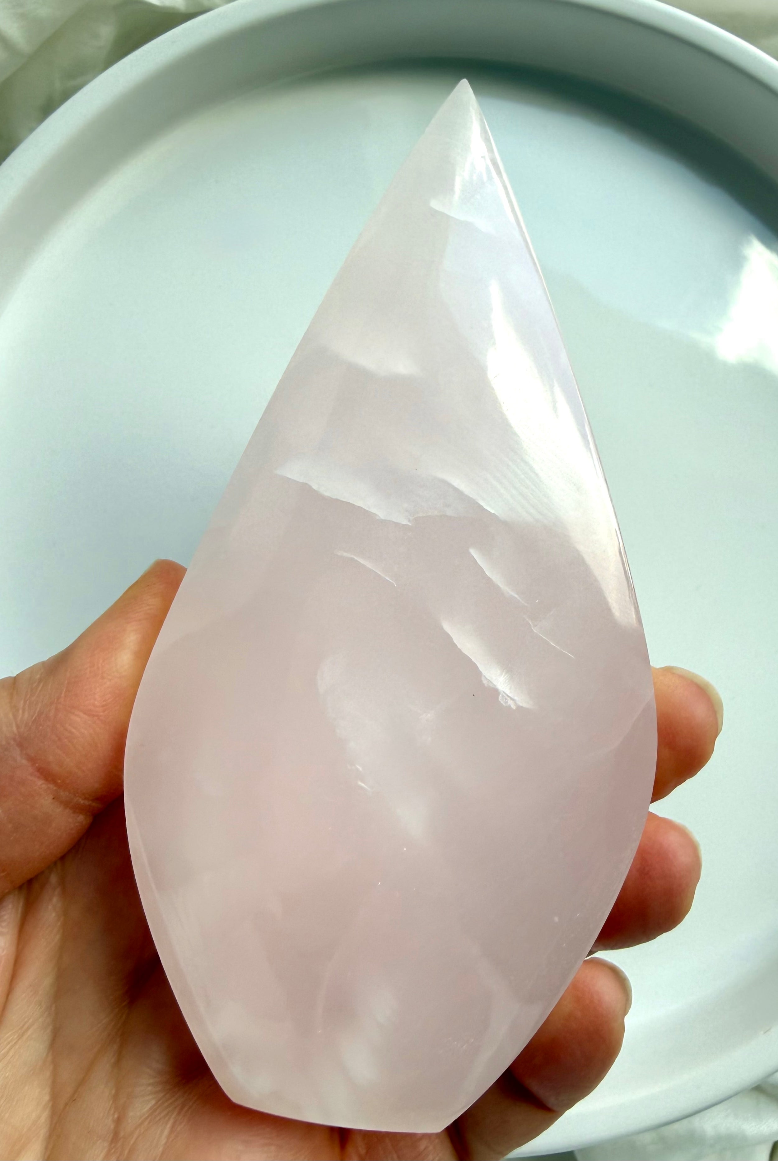 Mangano Calcite flame crystal held in hand for scale, featuring soft pink translucency and a smooth polished finish from Pakistan