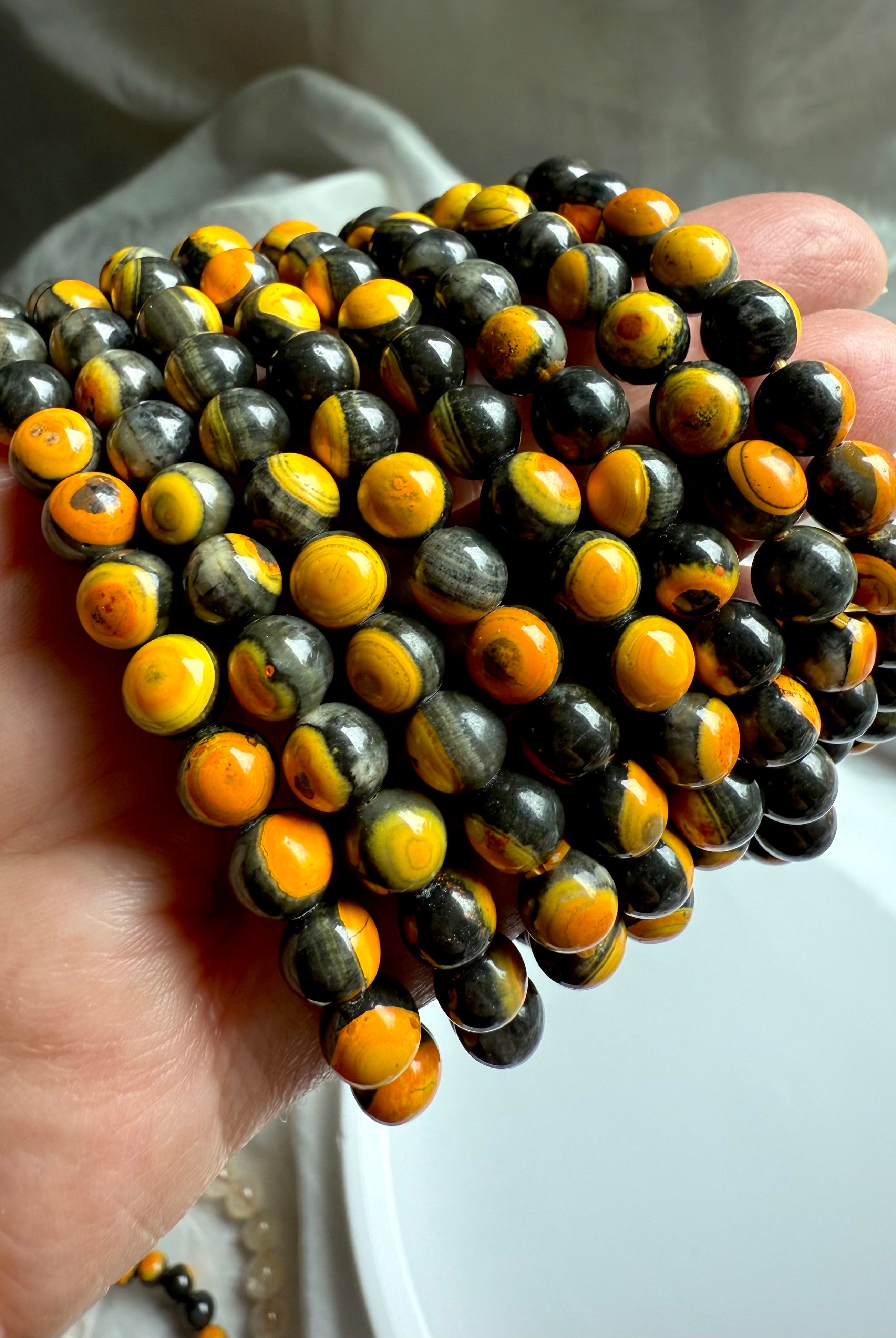 Group of bumblebee jasper crystal bracelets displayed in hand, rich orange and yellow banding in natural stone beads for motivation and energy