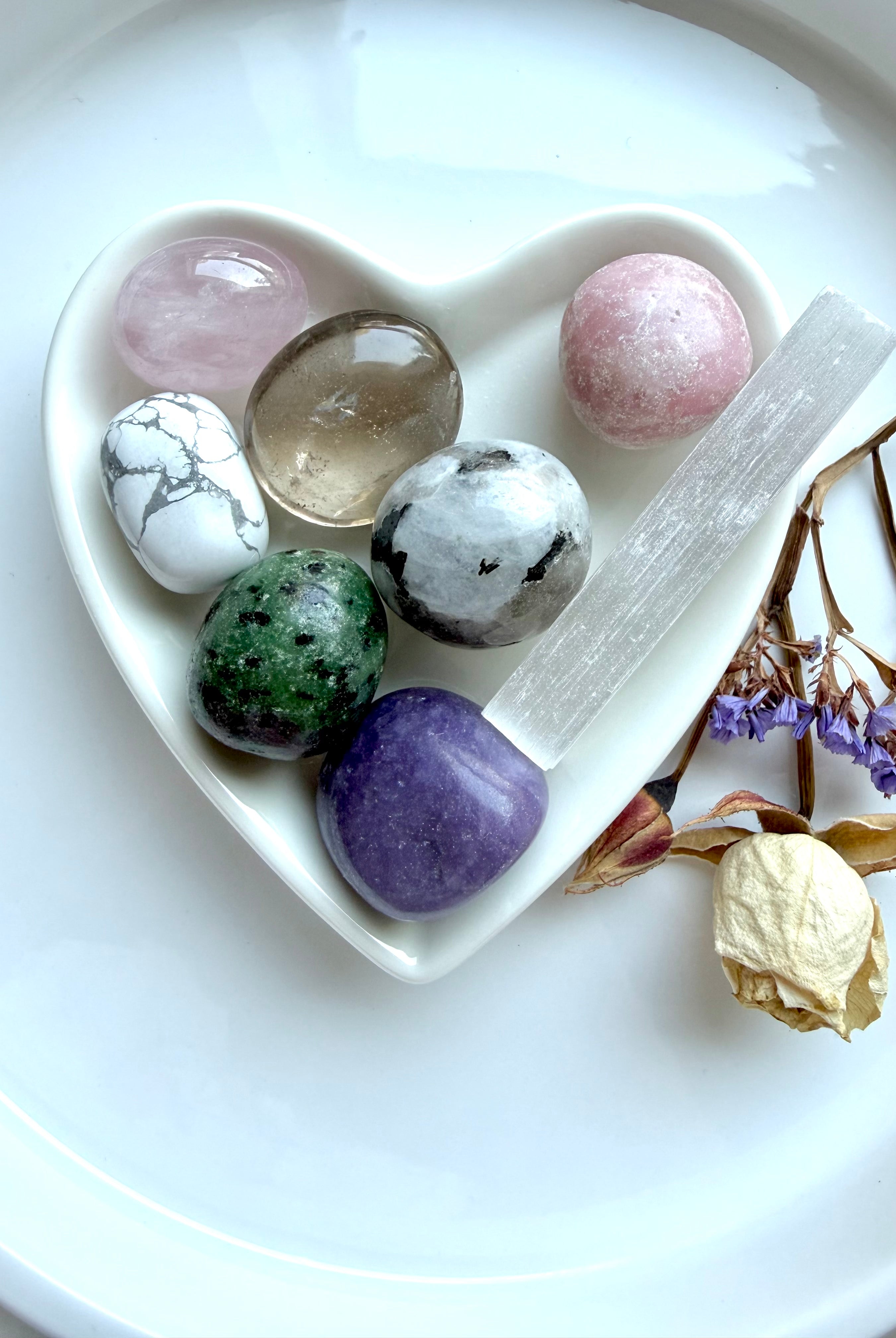 grief healing crystal gift set with seven comforting stones and selenite cleansing wand arranged in white heart-shaped bowl with dried flowers on white surface