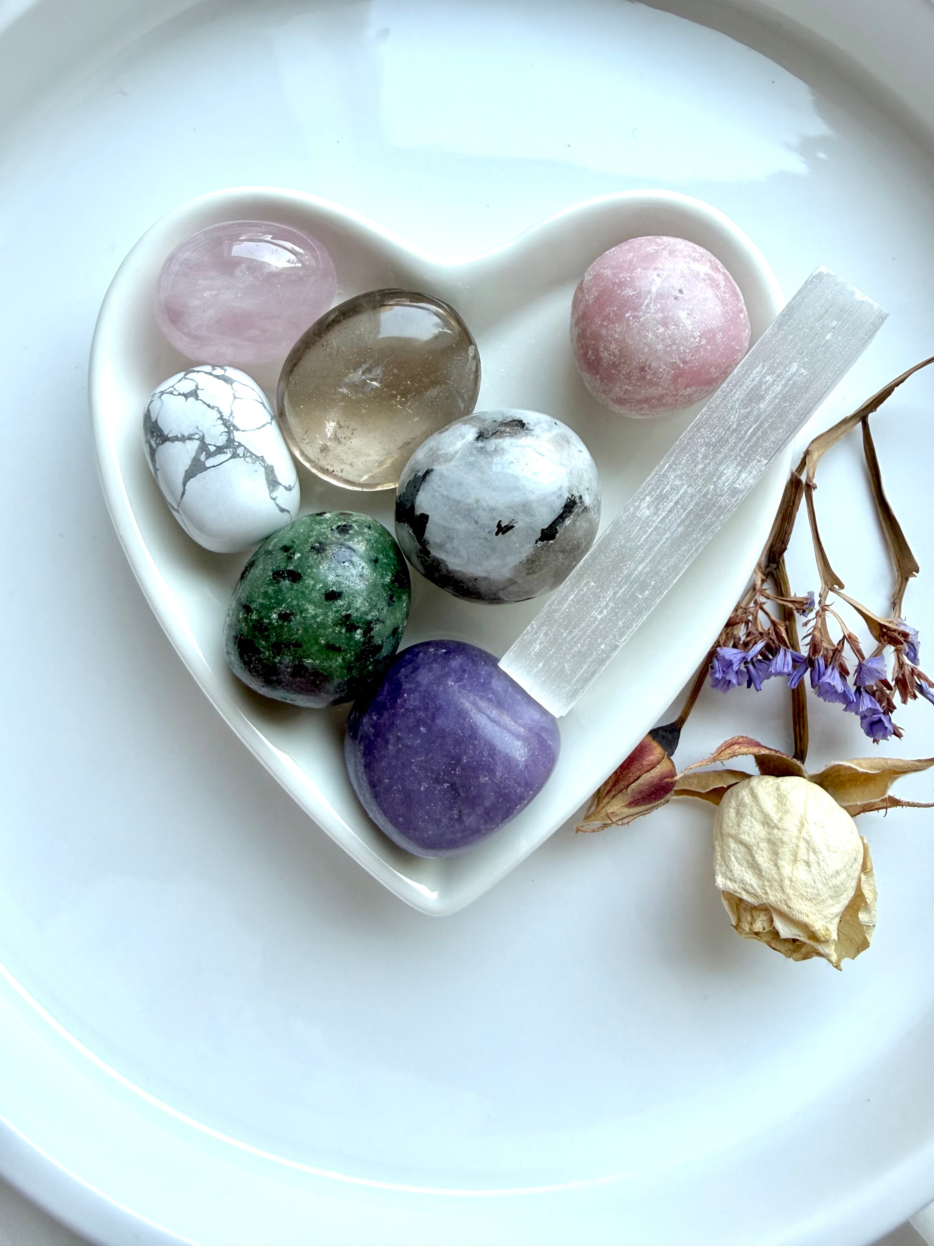 grief healing crystal gift set with seven comforting stones and selenite cleansing wand arranged in white heart-shaped bowl with dried flowers on white surface