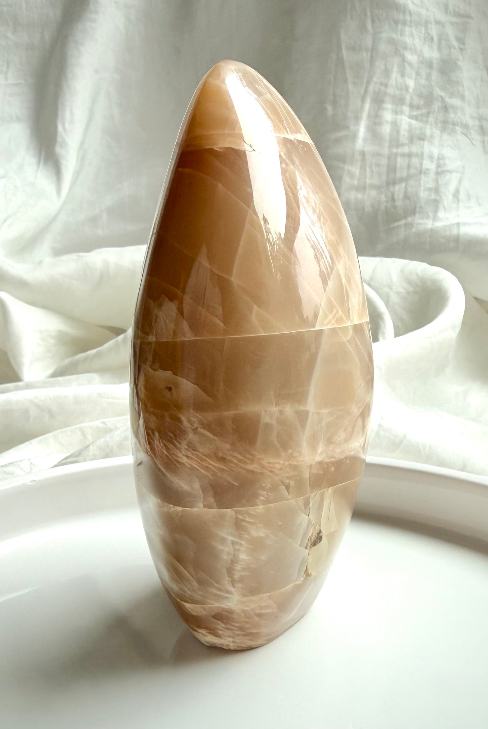 Side view of Peach Moonstone freeform crystal with soft shimmer and polished curved oval shape