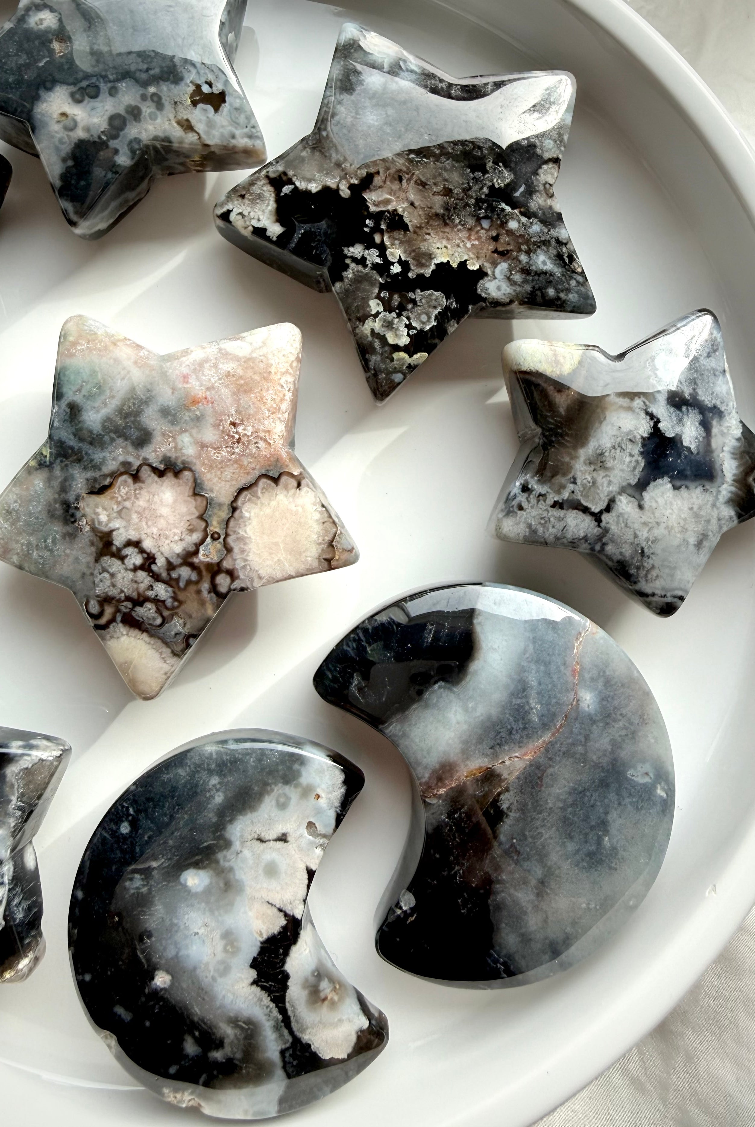 assortment of black flower agate moon and star crystals arranged together highlighting unique natural patterning