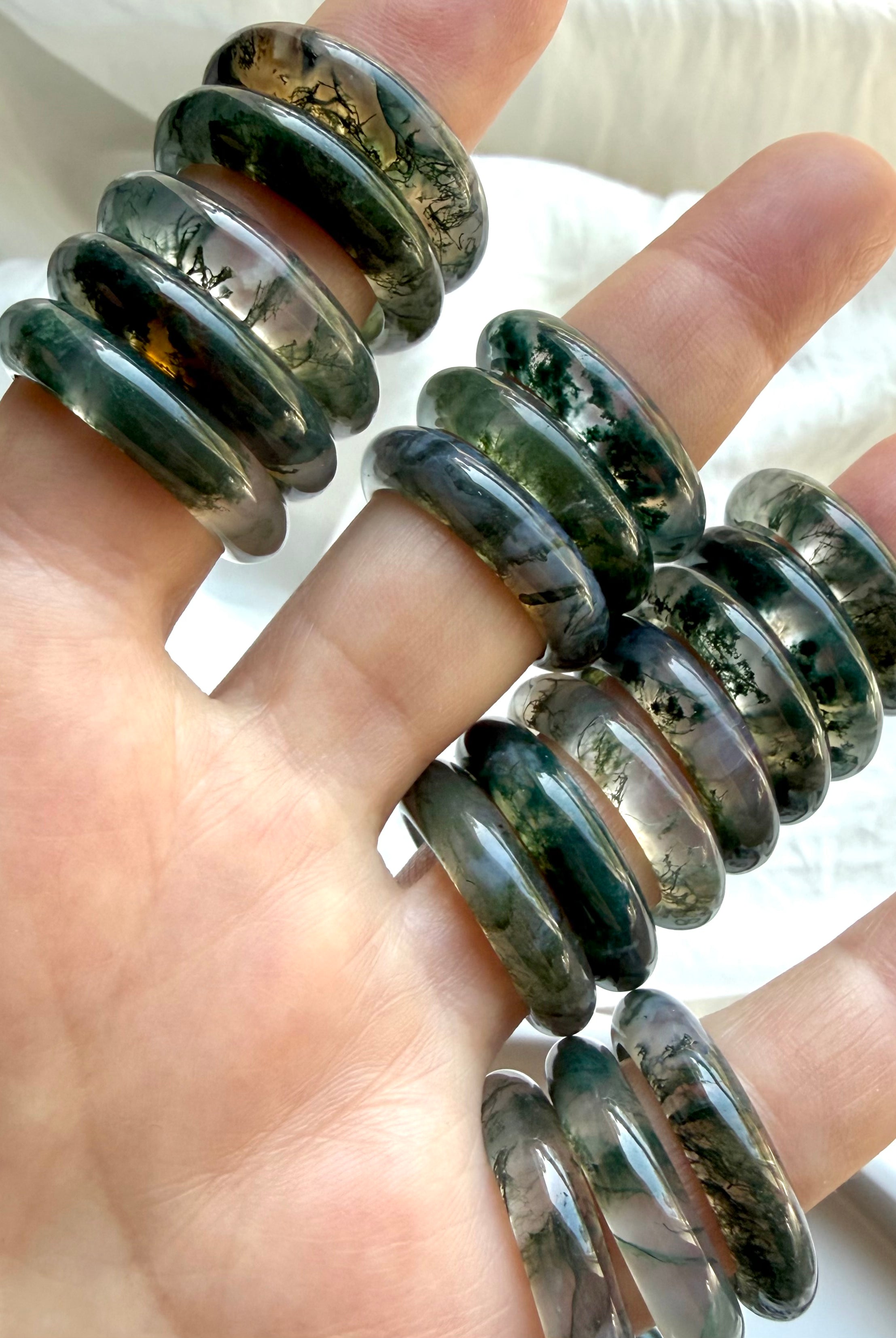 multiple moss agate band rings held in hand showing natural variation, polished crystal rings for balance growth and emotional healing