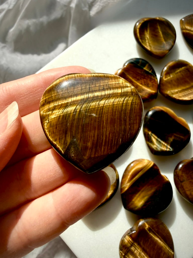 Golden Tiger’s Eye heart worry stones displayed in sunlight, showing natural chatoyancy and polished heart-shaped carvings