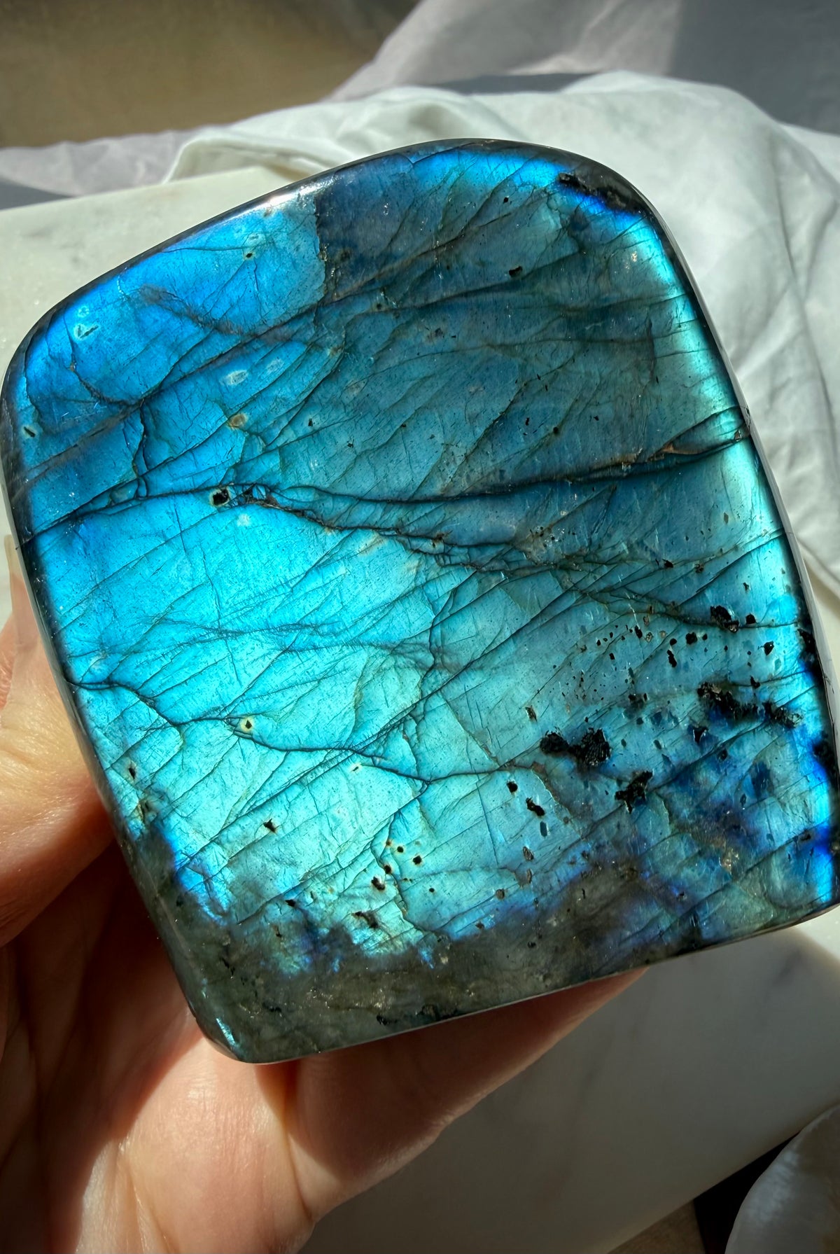 Electric blue Labradorite freeform held in hand showing vibrant aqua-blue flash and polished surface