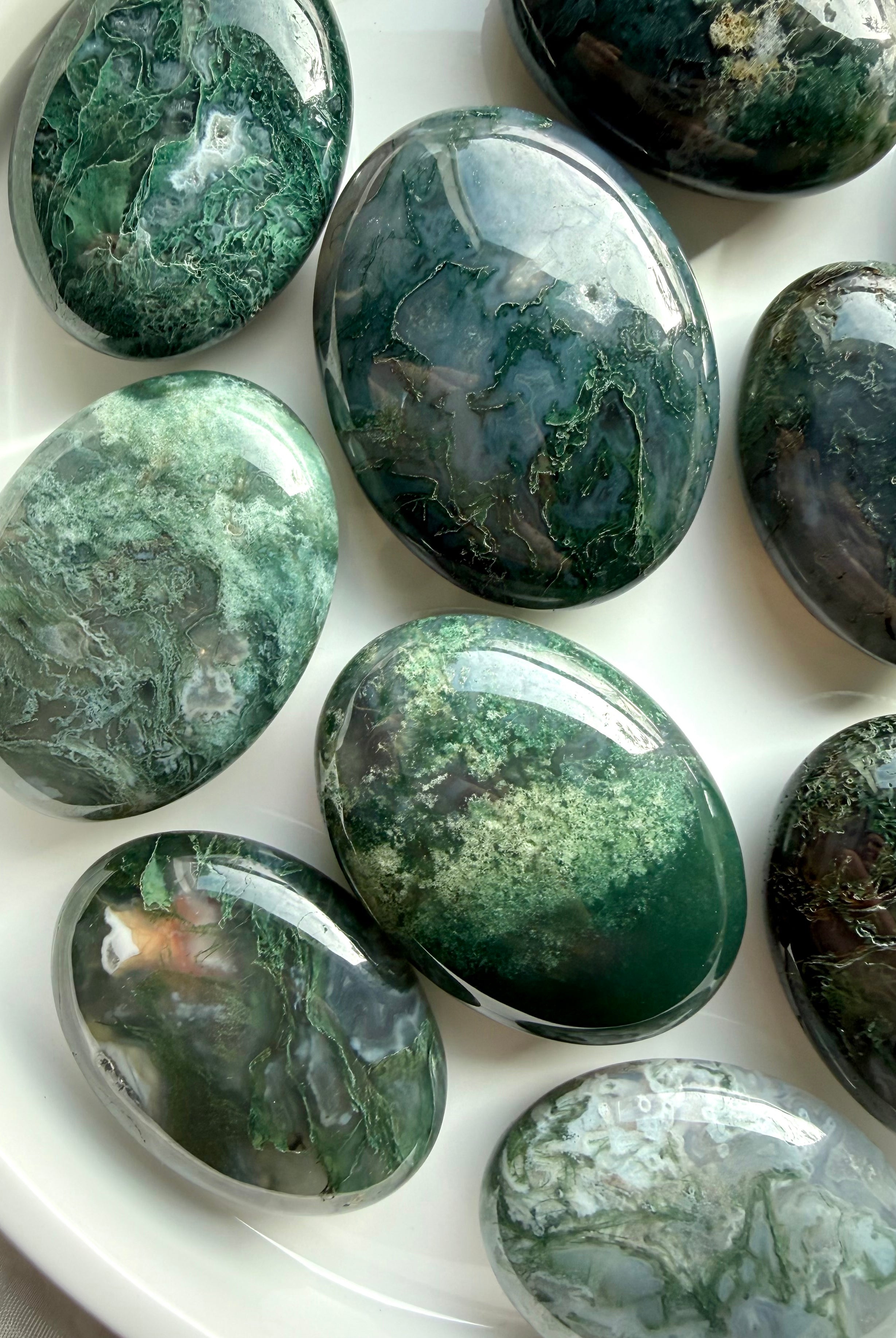 Assorted moss agate palm stones on white tray, calming green crystals for grounding and emotional balance