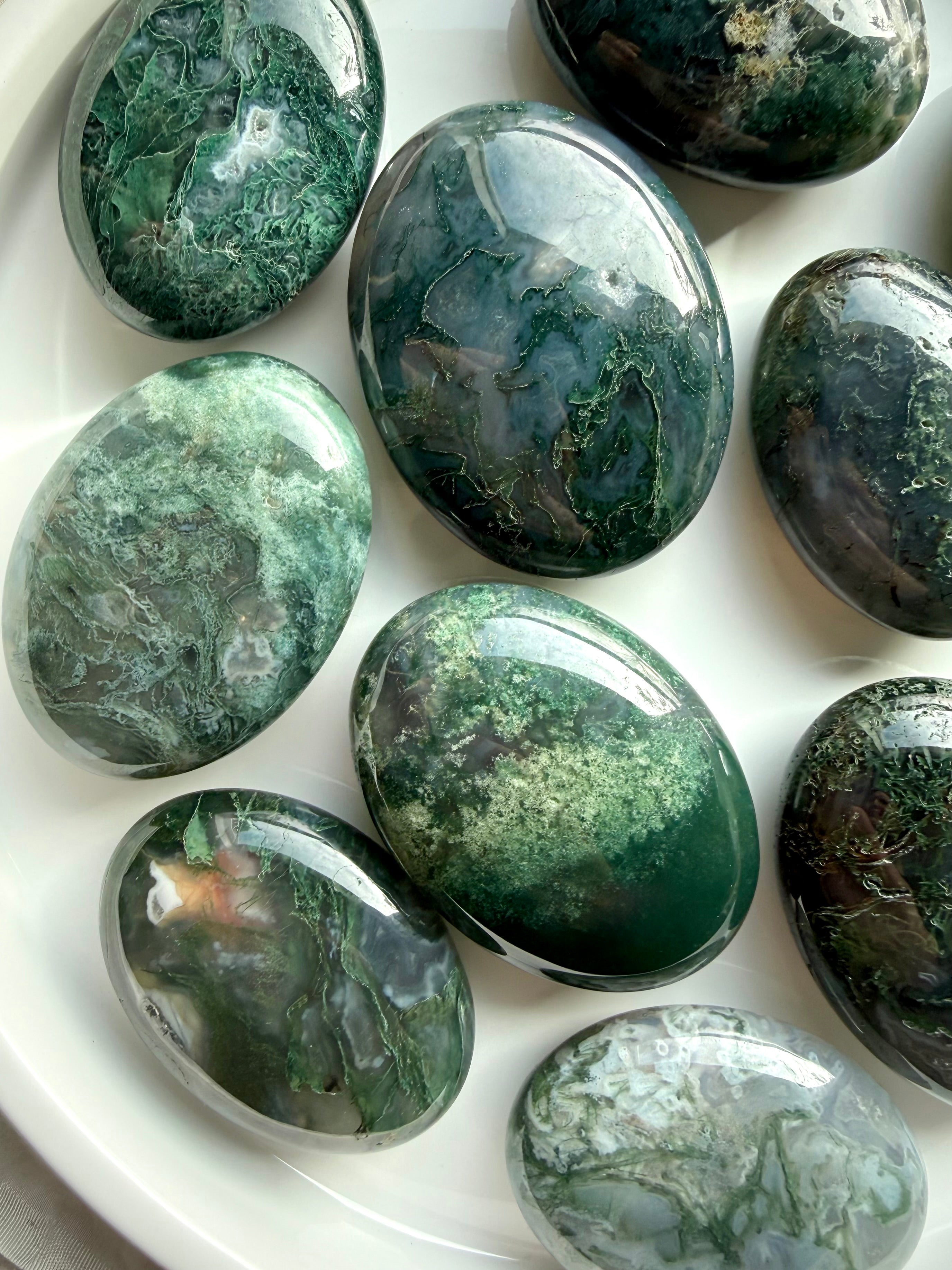 Assorted moss agate palm stones on white tray, calming green crystals for grounding and emotional balance