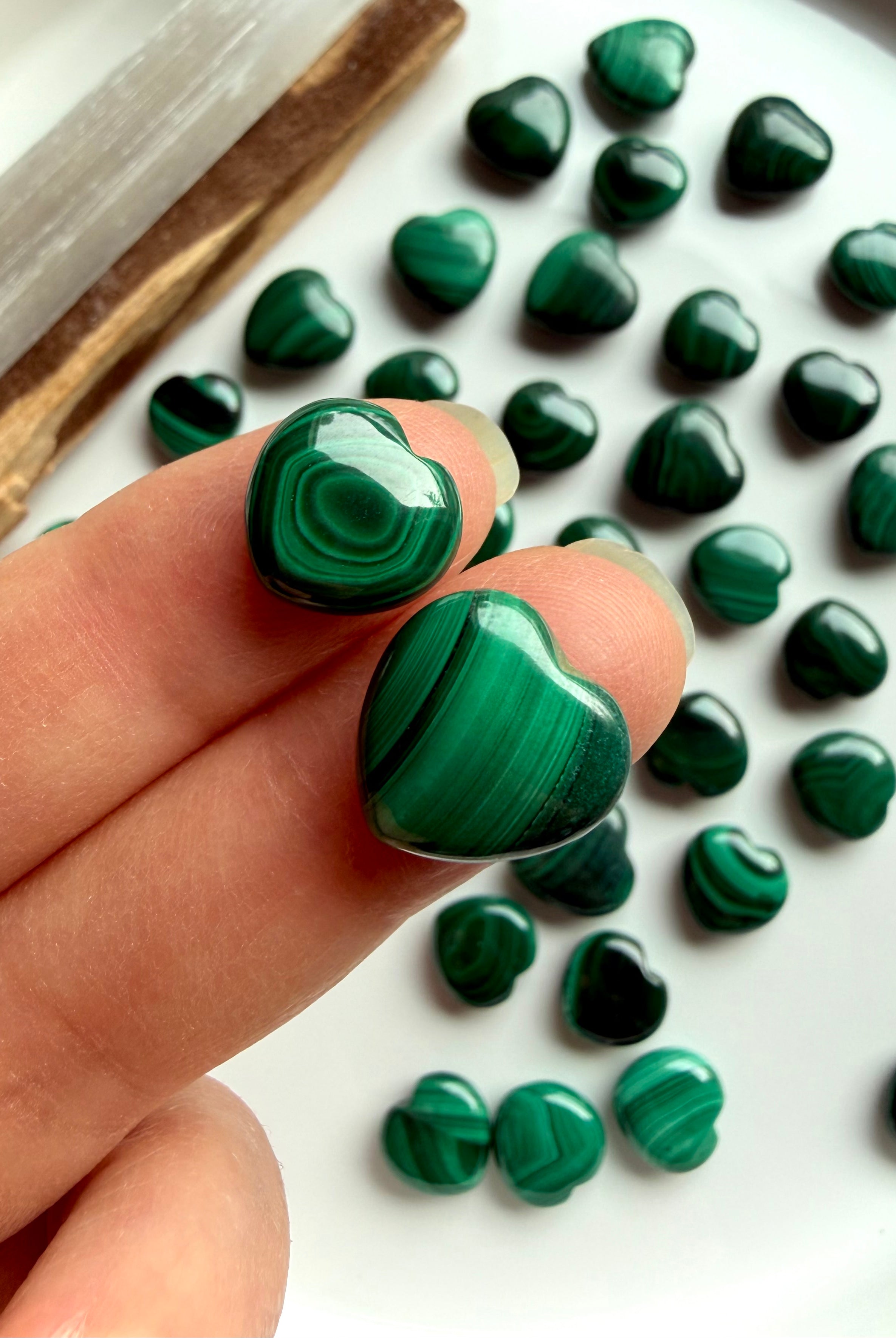 Two Malachite mini heart carvings held on my fingertips to show size and pattern detail.