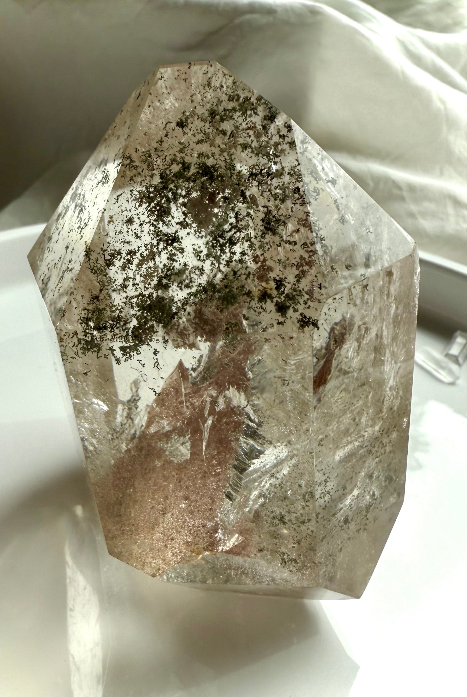 A self standing Lodolite Garden Quartz Crystal shown on a white plate photographed in natural light