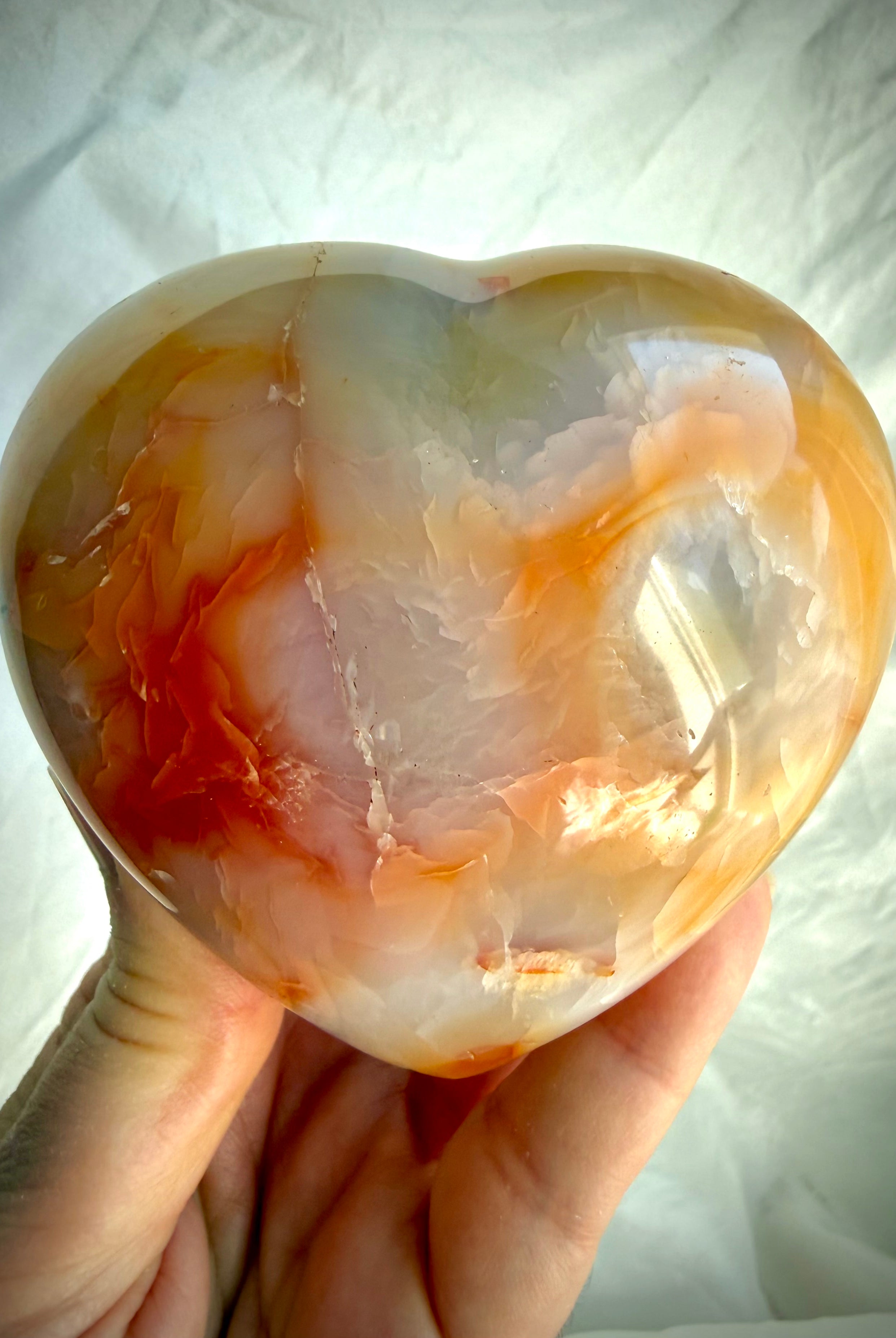 One-of-a-kind Carnelian heart crystal held in hand showing glossy polish, natural banding and scale