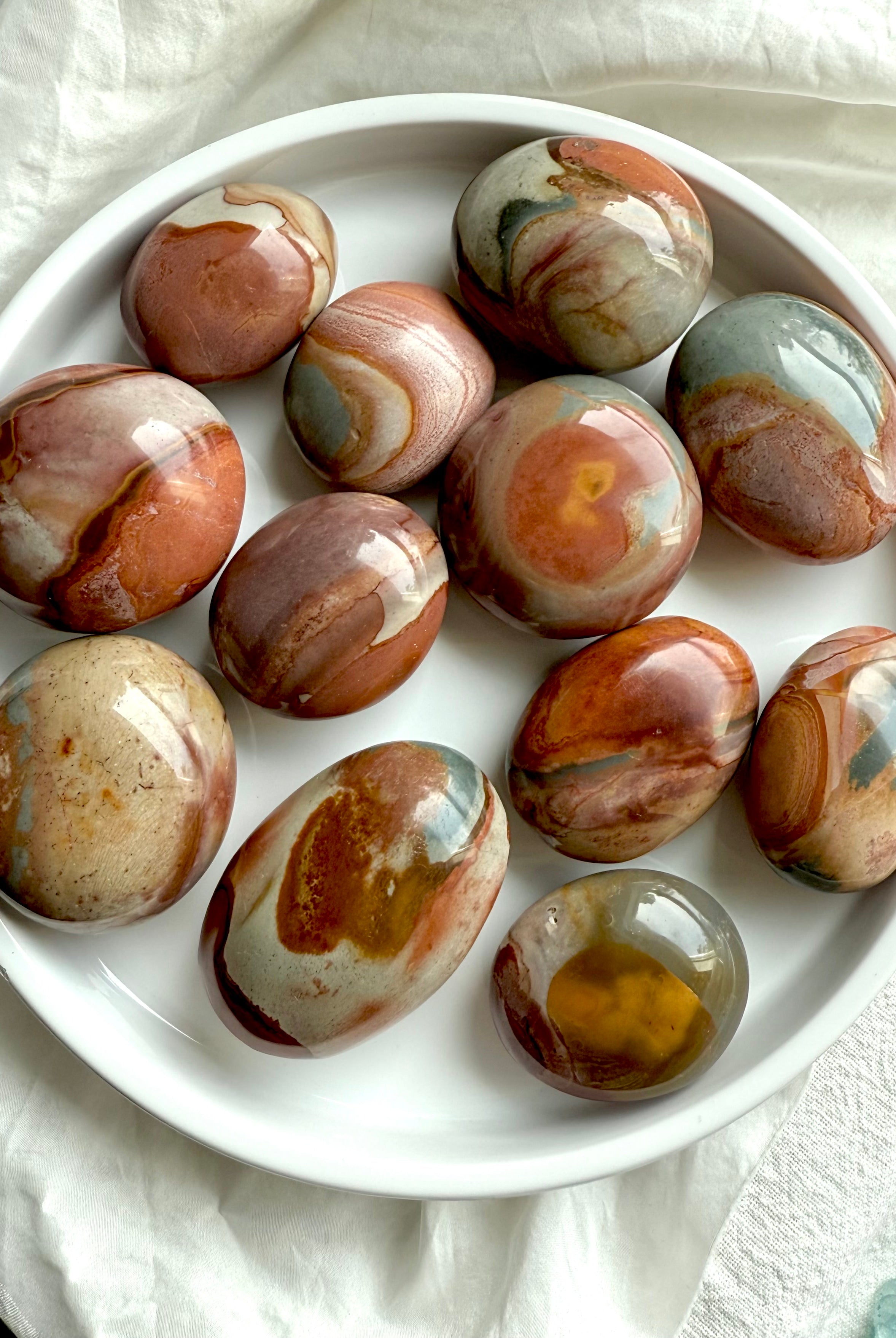 Earthy Polychrome Jasper palm stones on a plate, showcasing swirled color patterns & calming energy.