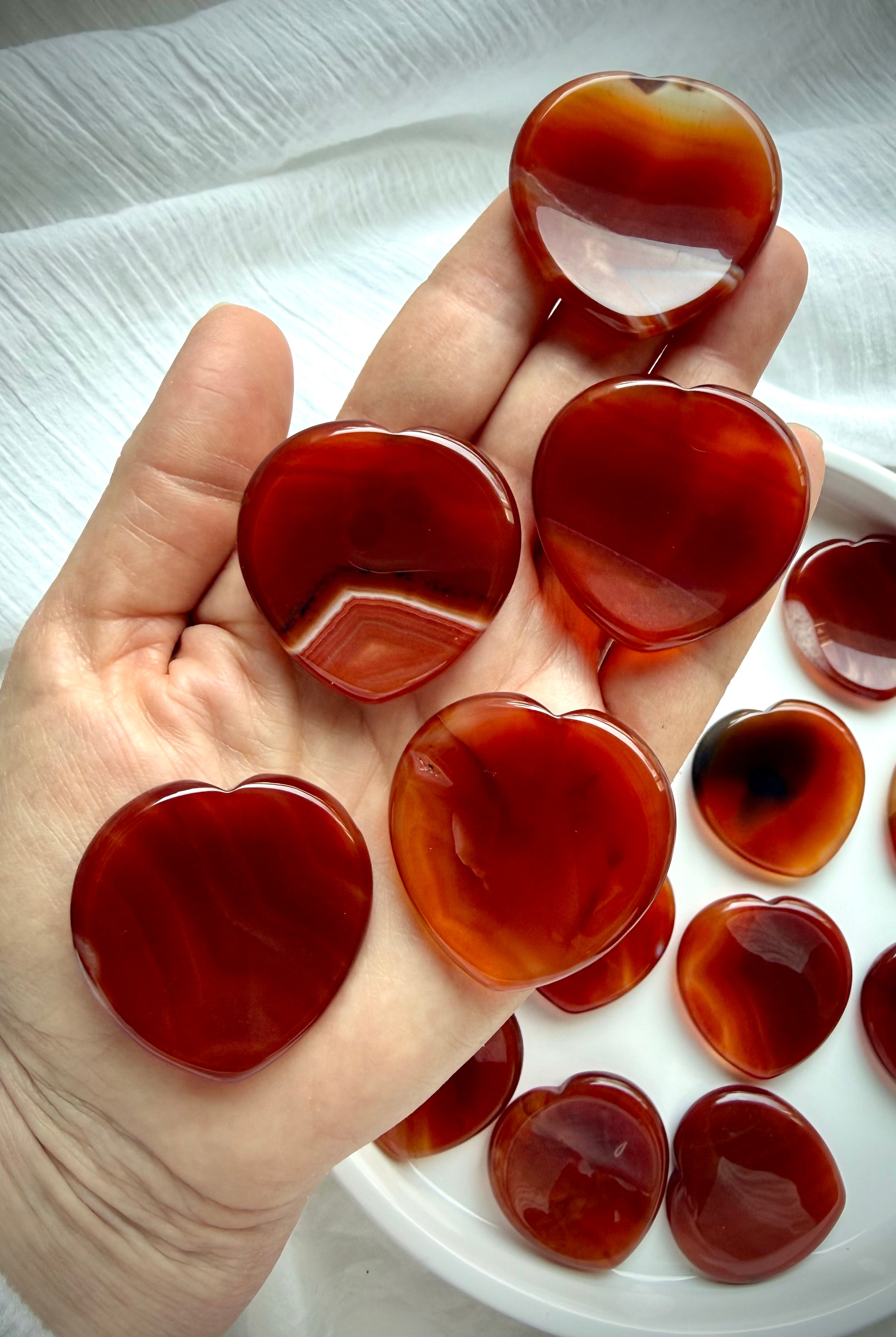 Carnelian heart worry stones held in hand showing natural color, translucency and pattern variation