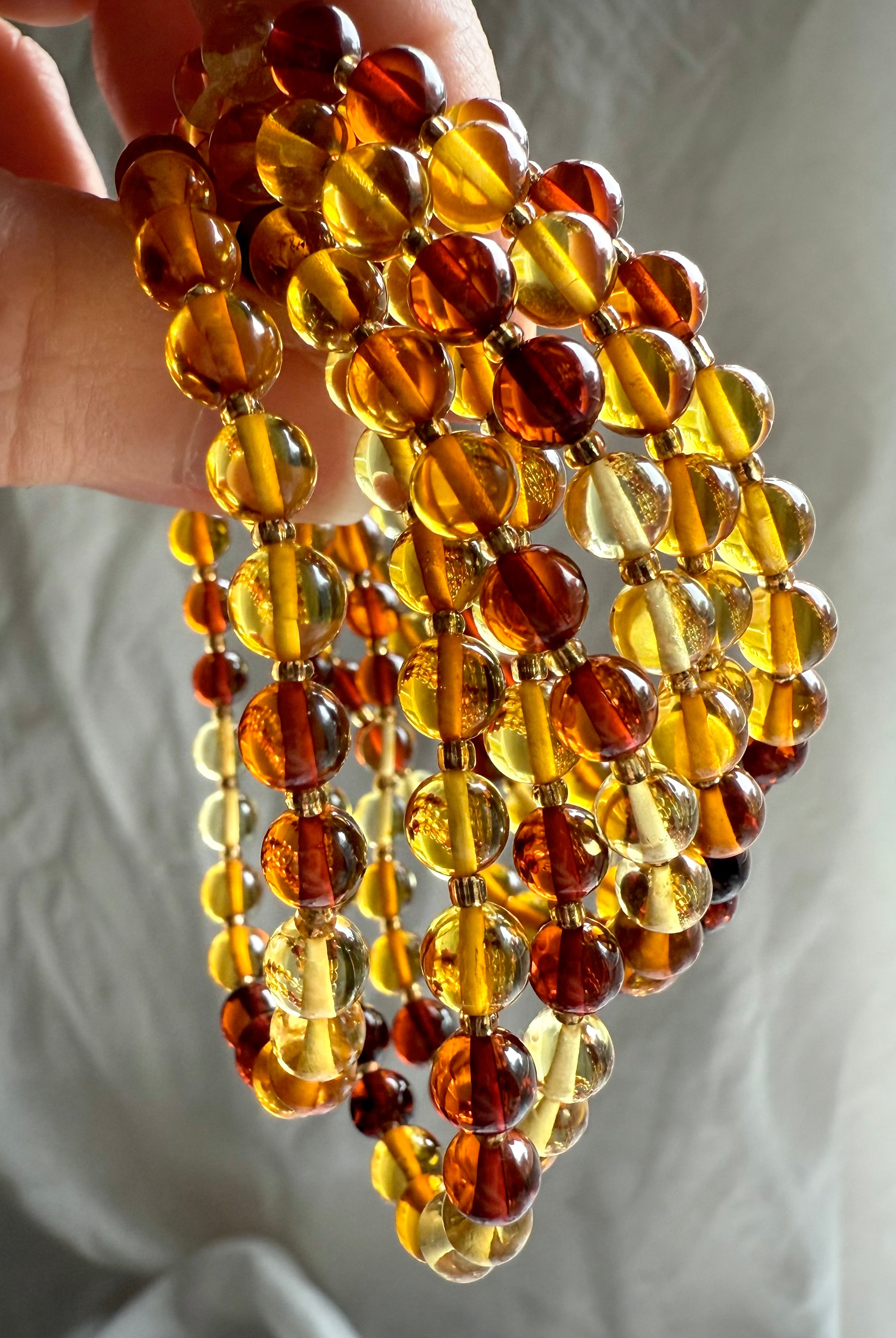 Hand holding strands of glowing amber bracelets in honey, cognac, and golden hues – Solar Plexus crystal for vitality and light