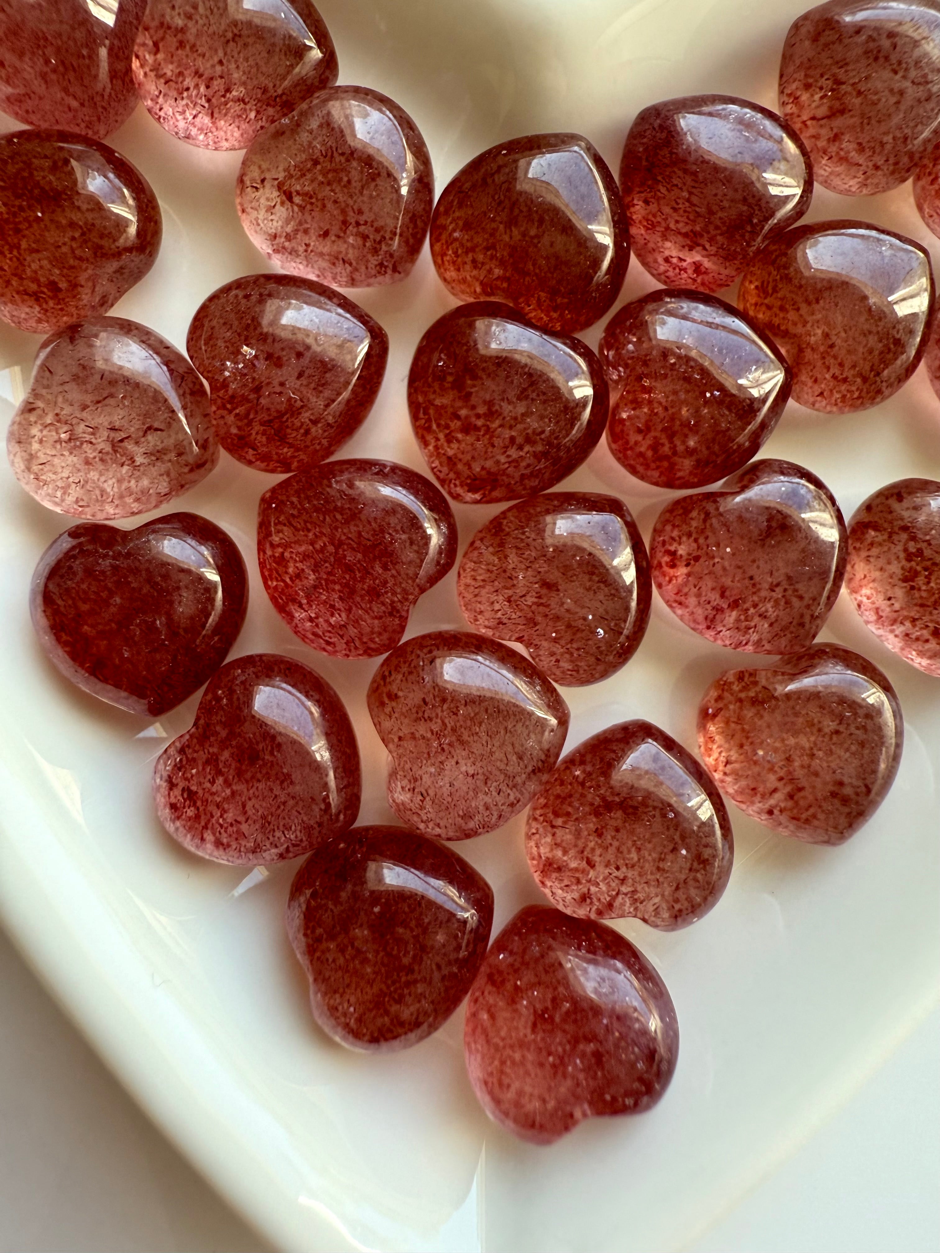 Closeup of Strawberry Quartz hearts on a white surface showing sparkle and natural inclusions.