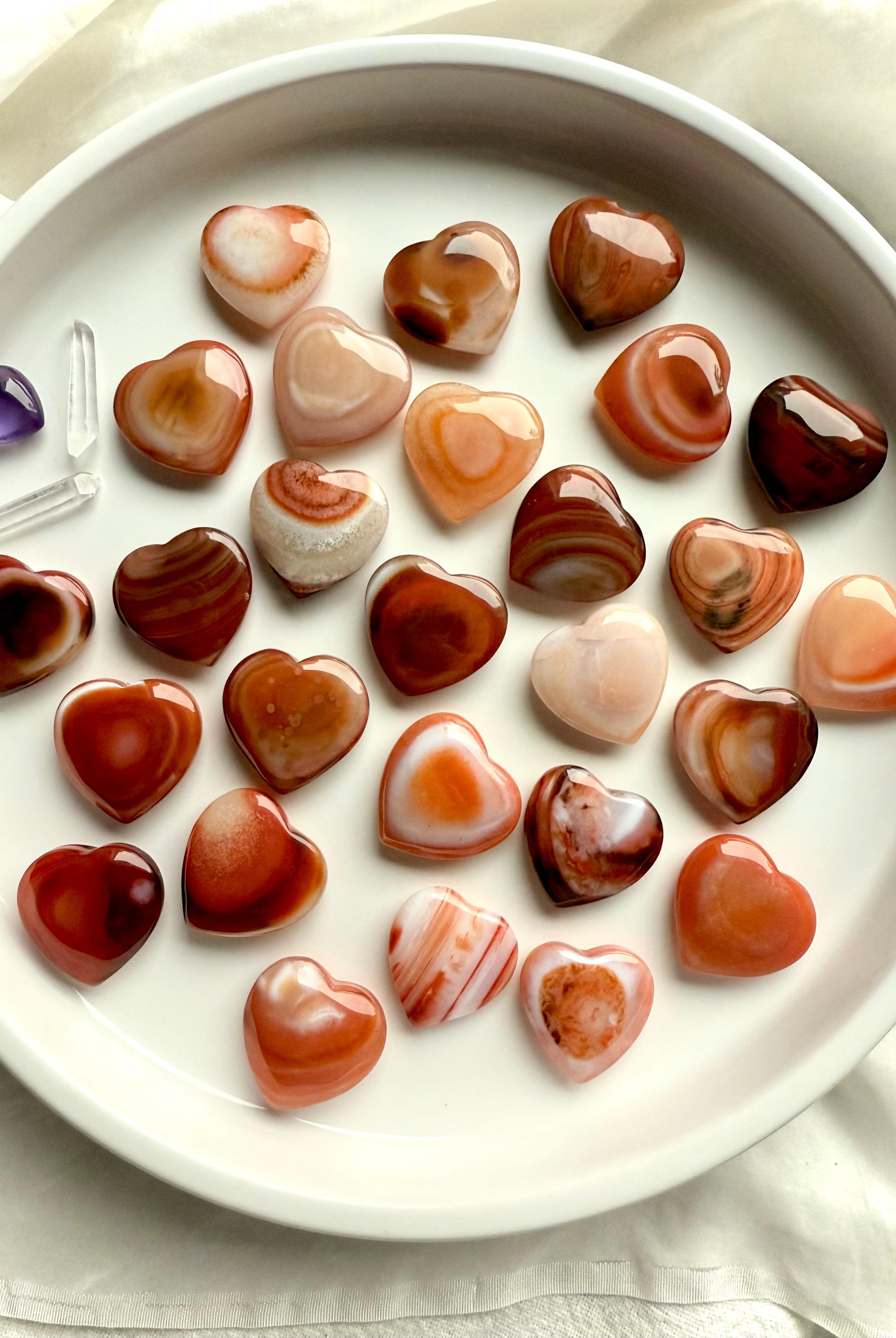 Assorted mini Carnelian heart carvings with rich orange, red, and cream banding, polished sacral chakra crystals for joy and inspired action