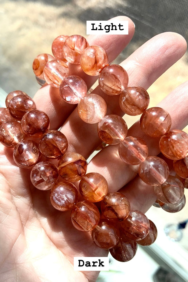 Four Hematoid Quartz bracelets in hand, showing two light and two dark Fire Quartz styles labeled for comparison