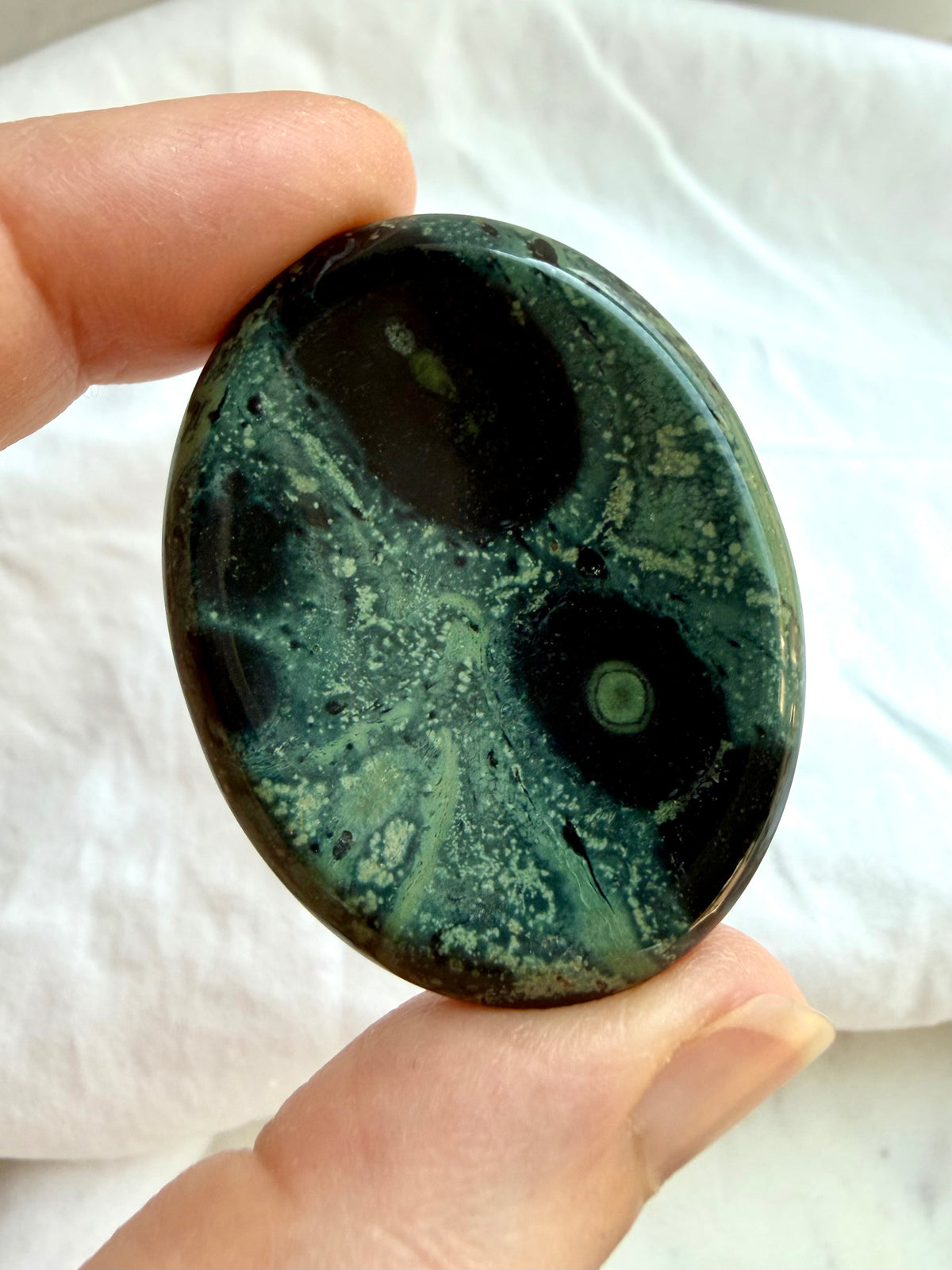 Close-up Kambaba Jasper worry stone showing forest and sage green color, black markings, and intricate orbicular patterns