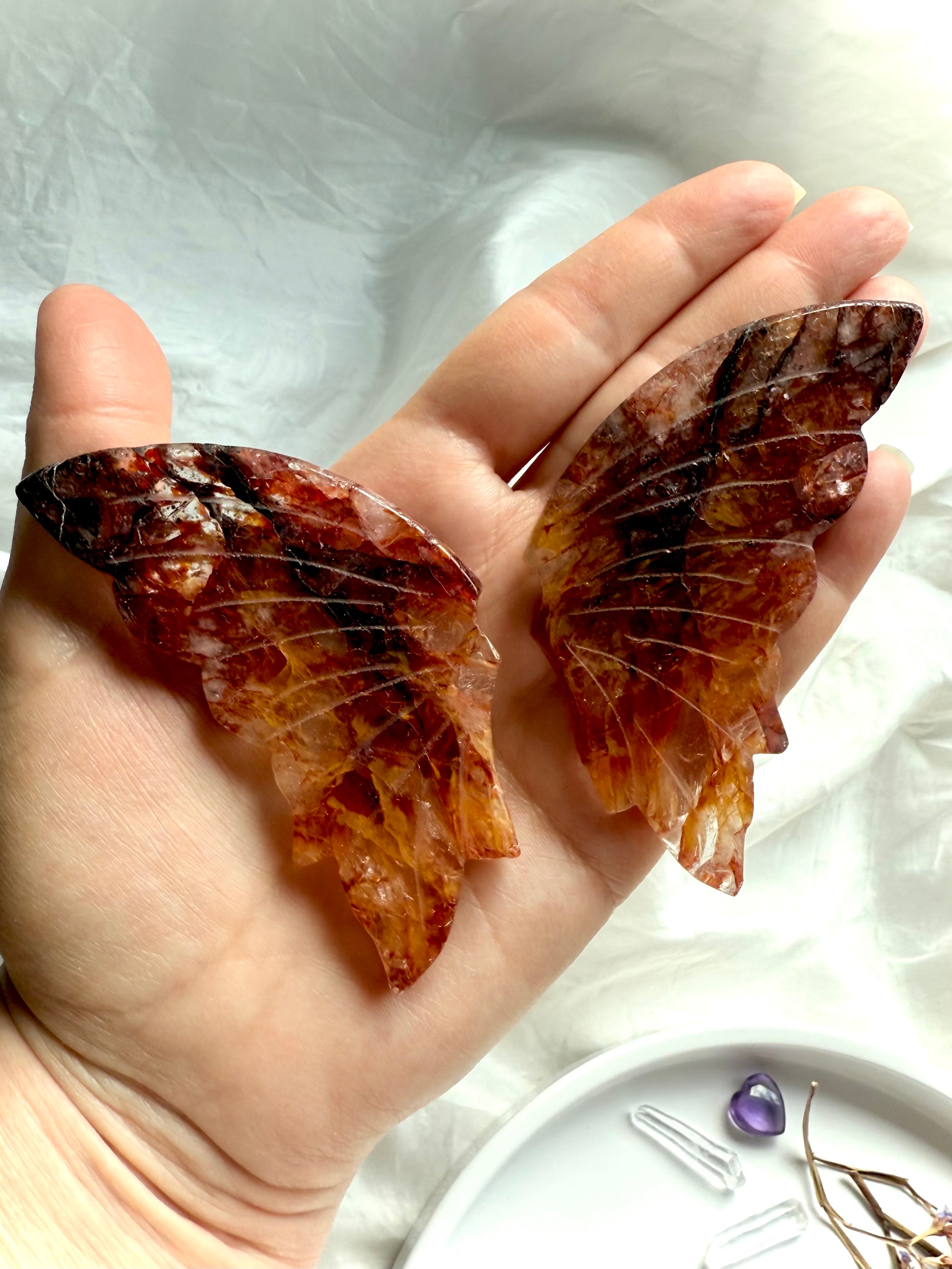 Hand holding carved Fire Quartz wings, showing size, shape, and the stone’s golden healer patterns.