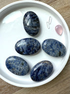 An array of high quality blue Sodalite Palm Stones shown on a white plate