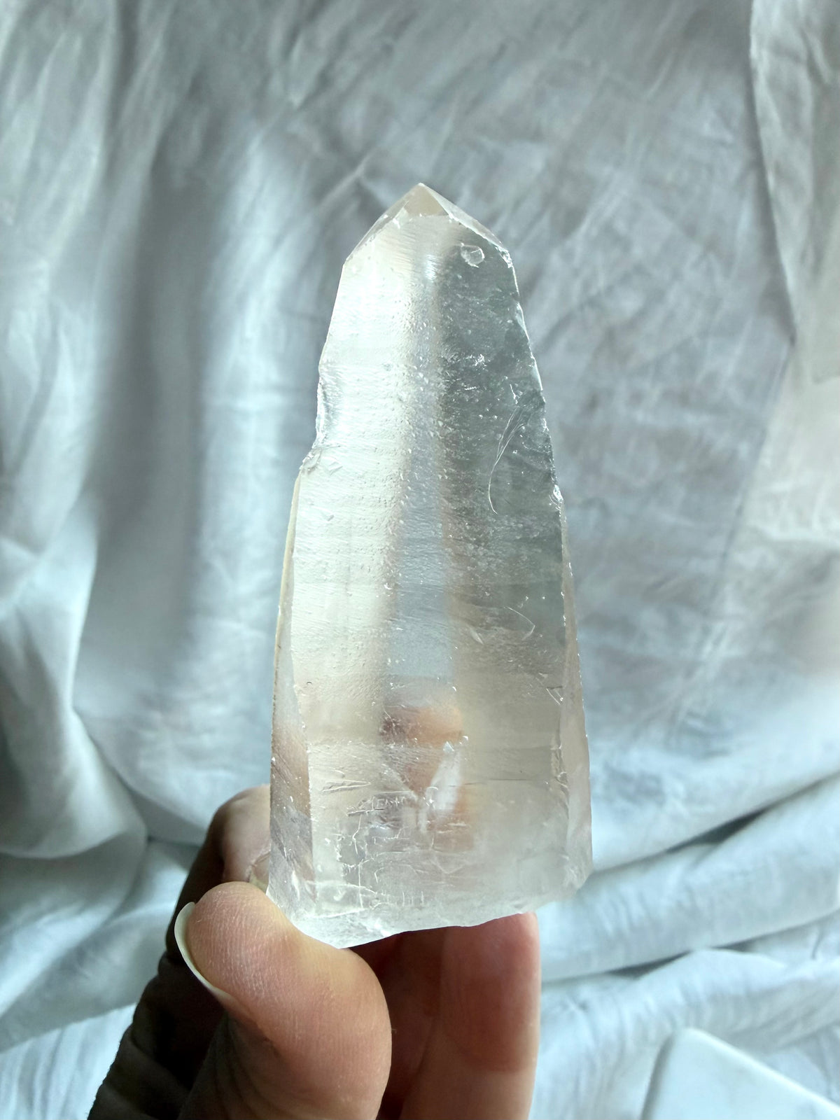 Large Lemurian Quartz point held in hand showing natural ladder lines, internal veils, and a clear crystal termination
