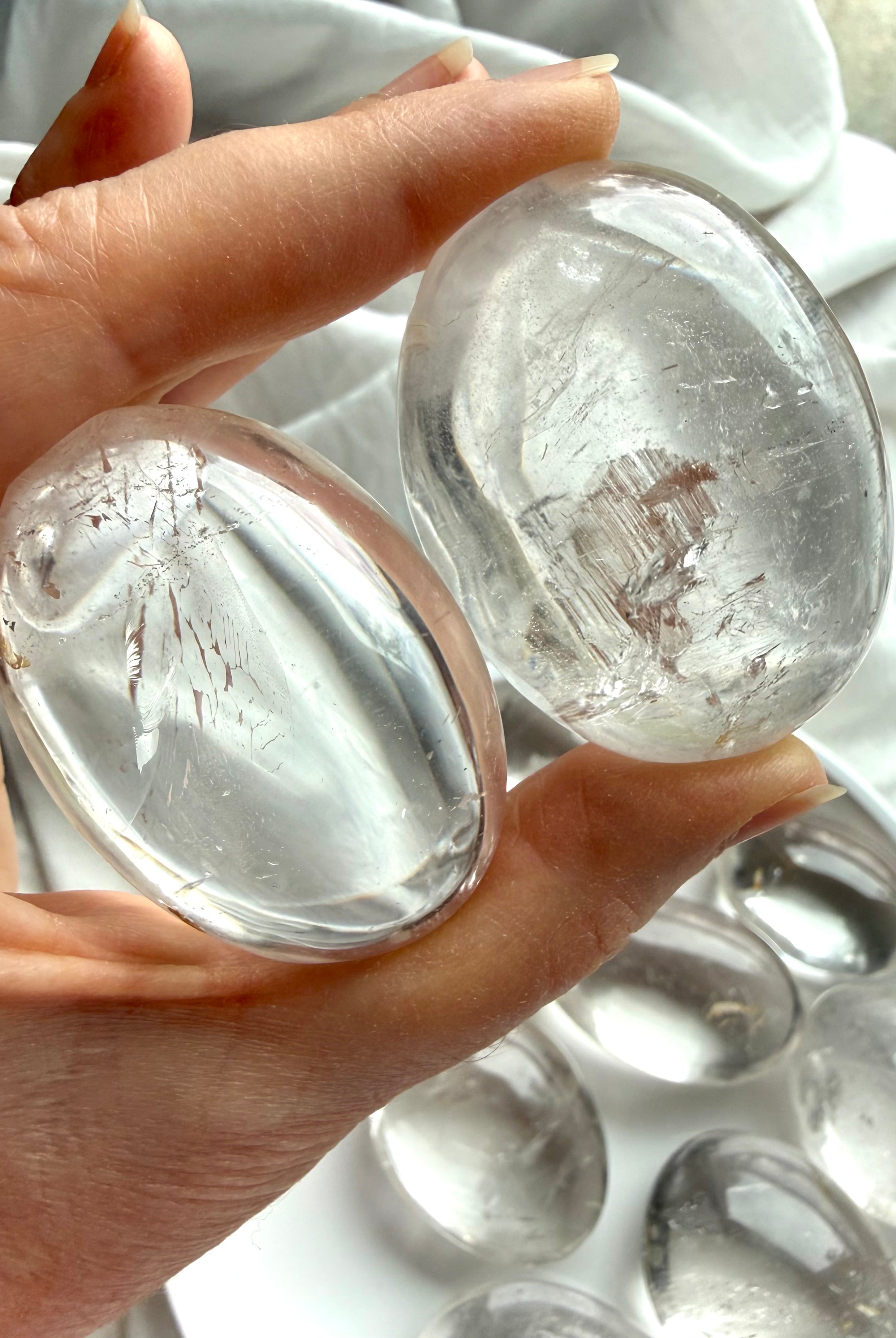 Two clear quartz palm stones close up, held to the light showing high clarity, internal veils & flashes